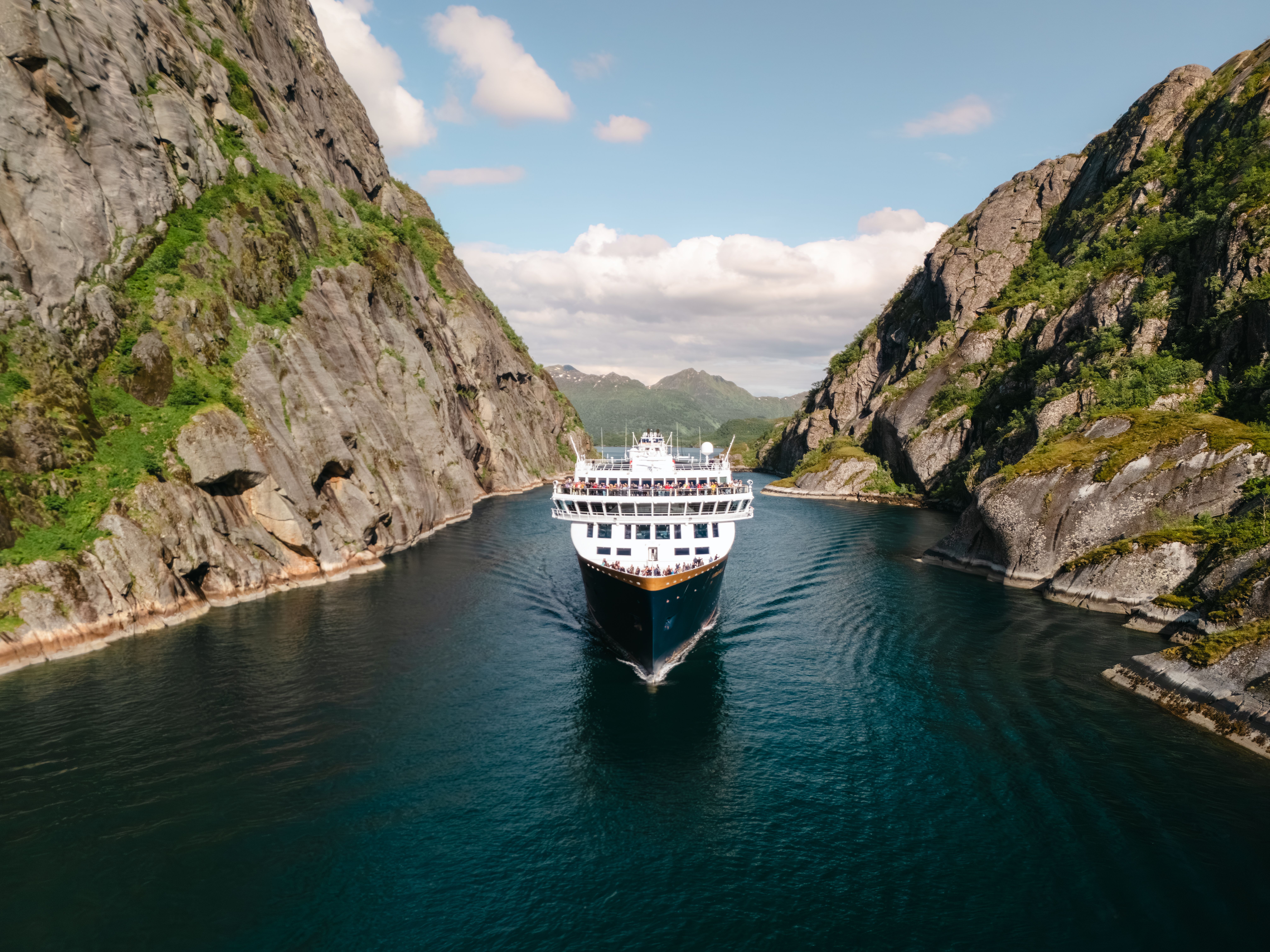 Havila-skip seiler mellom de bratte fjellveggene i Trollfjorden om sommeren