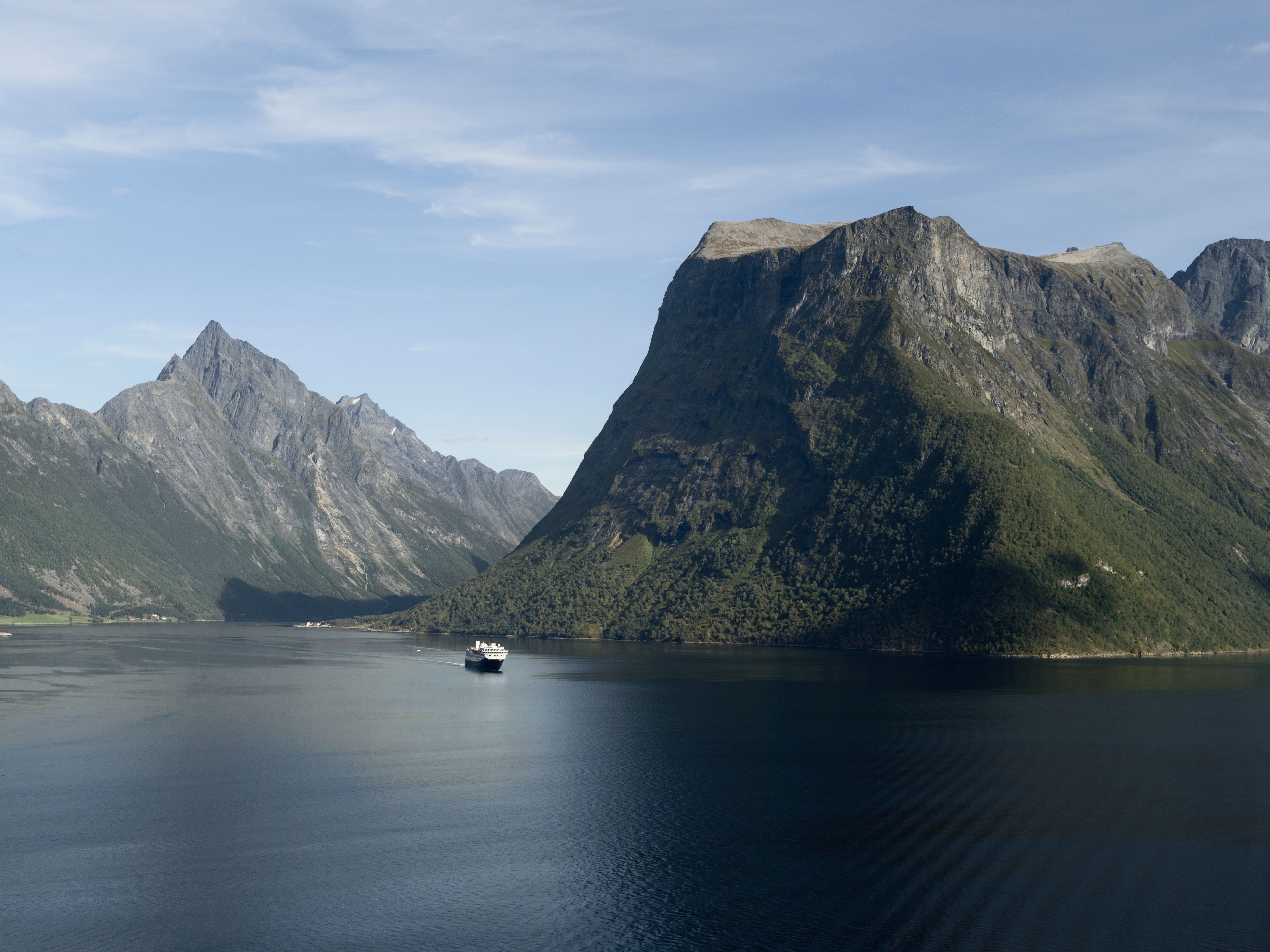 Havila-fartyg som seglar genom Hjørundfjorden, omgivet av snötäckta toppar, vattenfall och dramatisk fjordnatur.