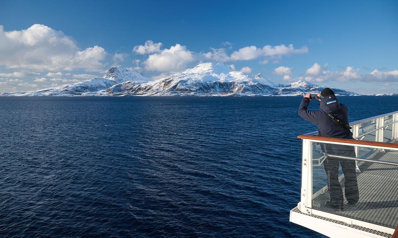 Guest photographing snow-covered mountains along the Norwegian coast from the deck of a Havila ship.