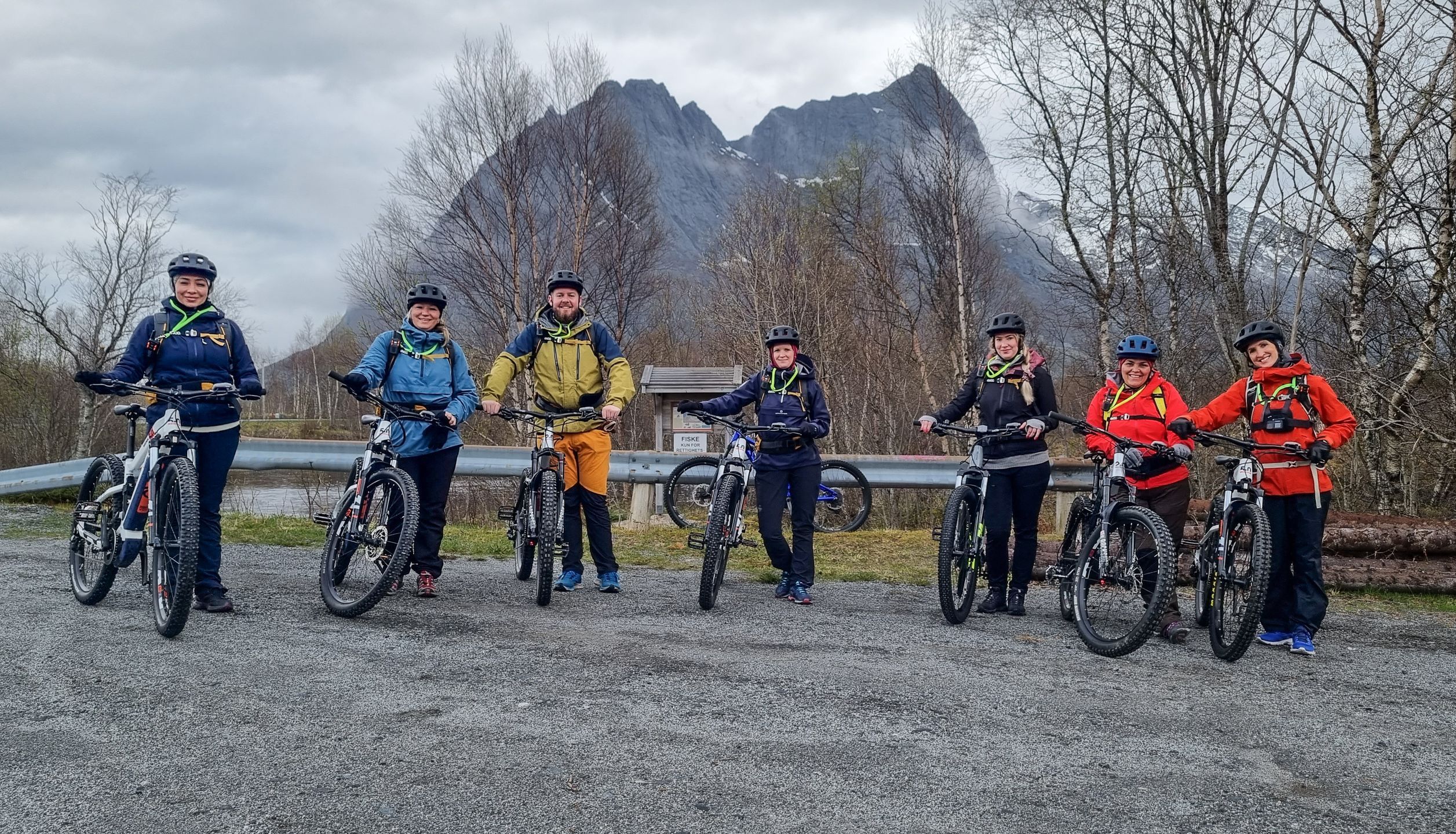 Sju syklister med elsykler foran en steinete fjelltopp på en elsykkeltur i Bodø, Norge