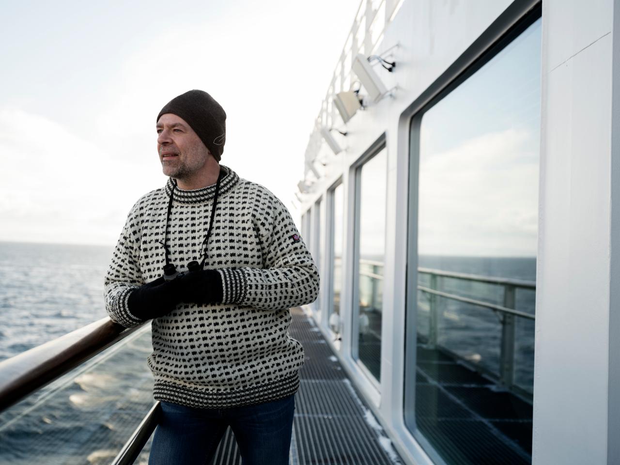 Gast in einem norwegischen Strickpullover, der an der Reling steht und aufs Meer blickt