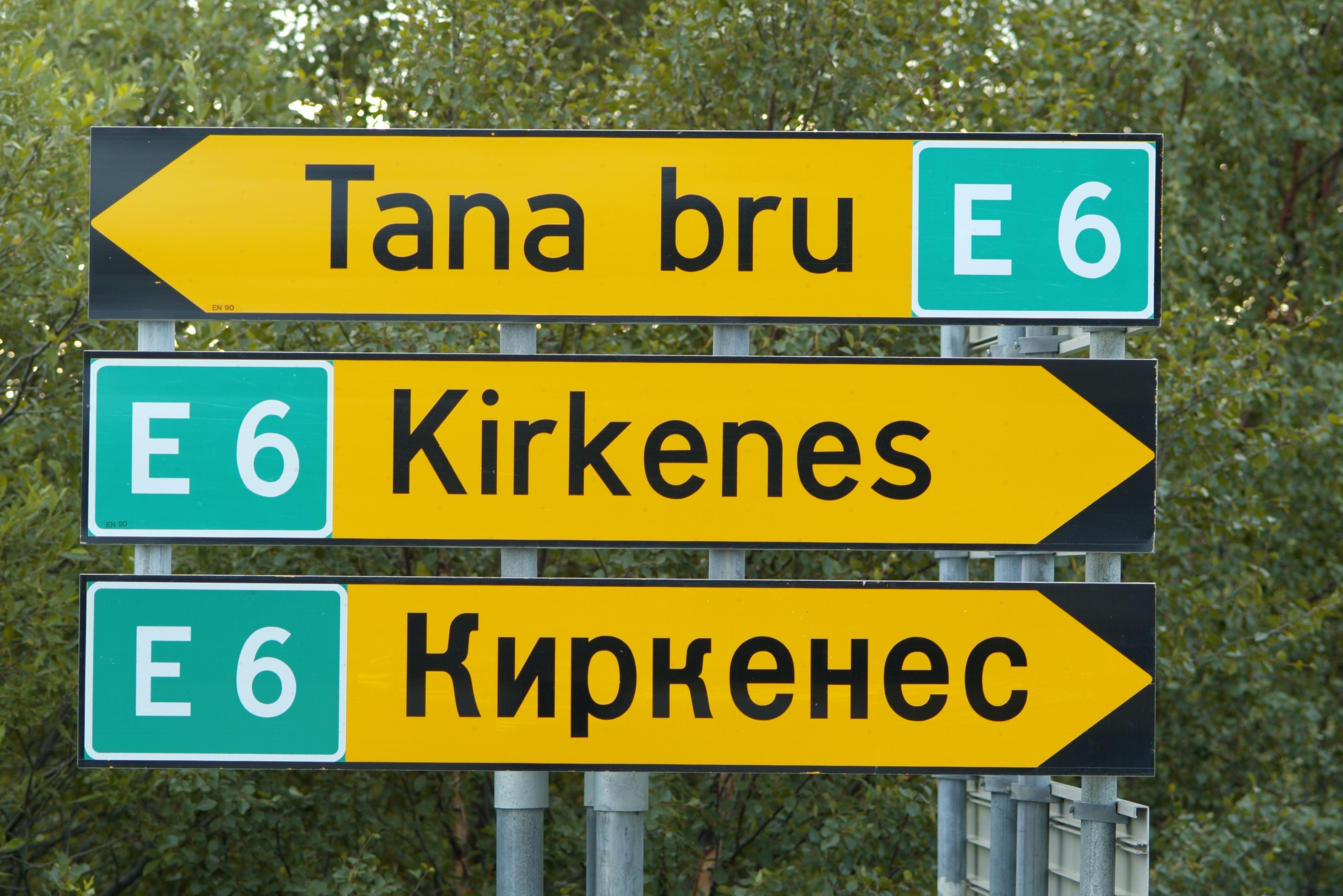 E6 road sign pointing to Kirkenes and Tana Bru in Northern Norway, with Norwegian and Russian place names.