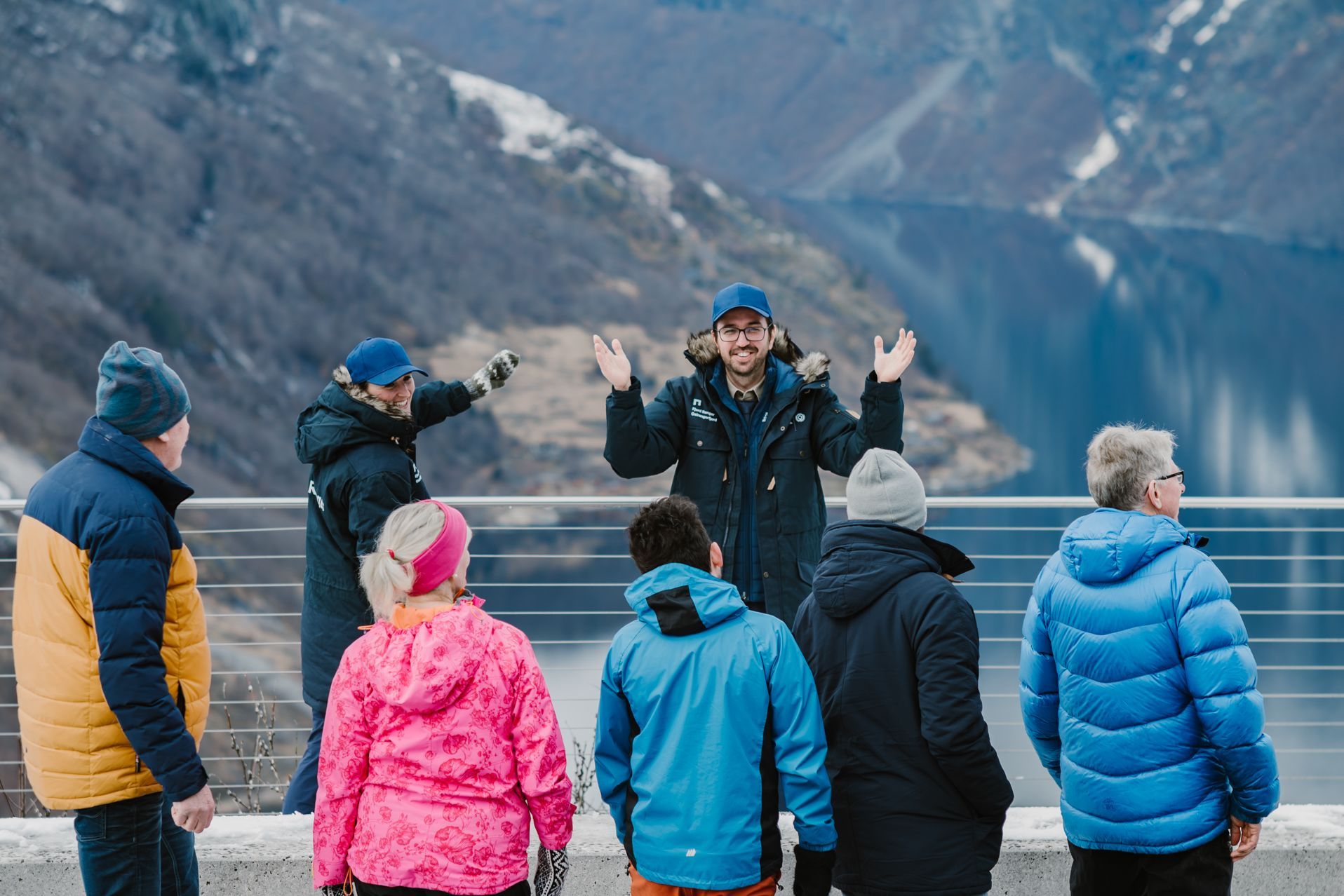 Zwei Fjord-Ranger-Führer begrüßen eine Reisegruppe an einem Aussichtspunkt des Geirangerfjords mit Bergen im Winter in Norwegen