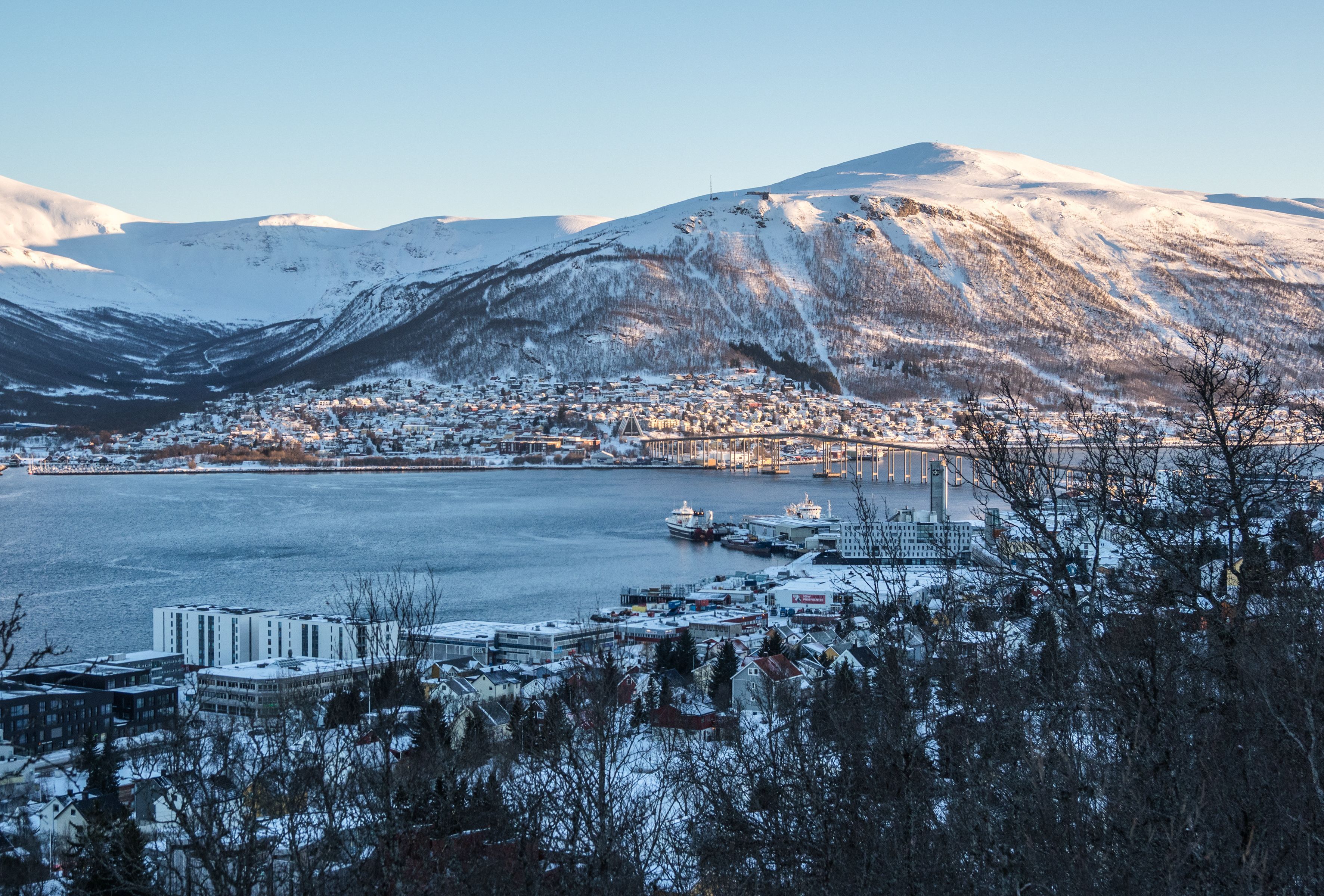 Panoramablick im Winter auf Tromsø mit seinem Hafen, dem Fjord und den schneebedeckten Bergen, gesehen von einem Aussichtspunkt während einer geführten arktischen Schneeschuhwanderung.