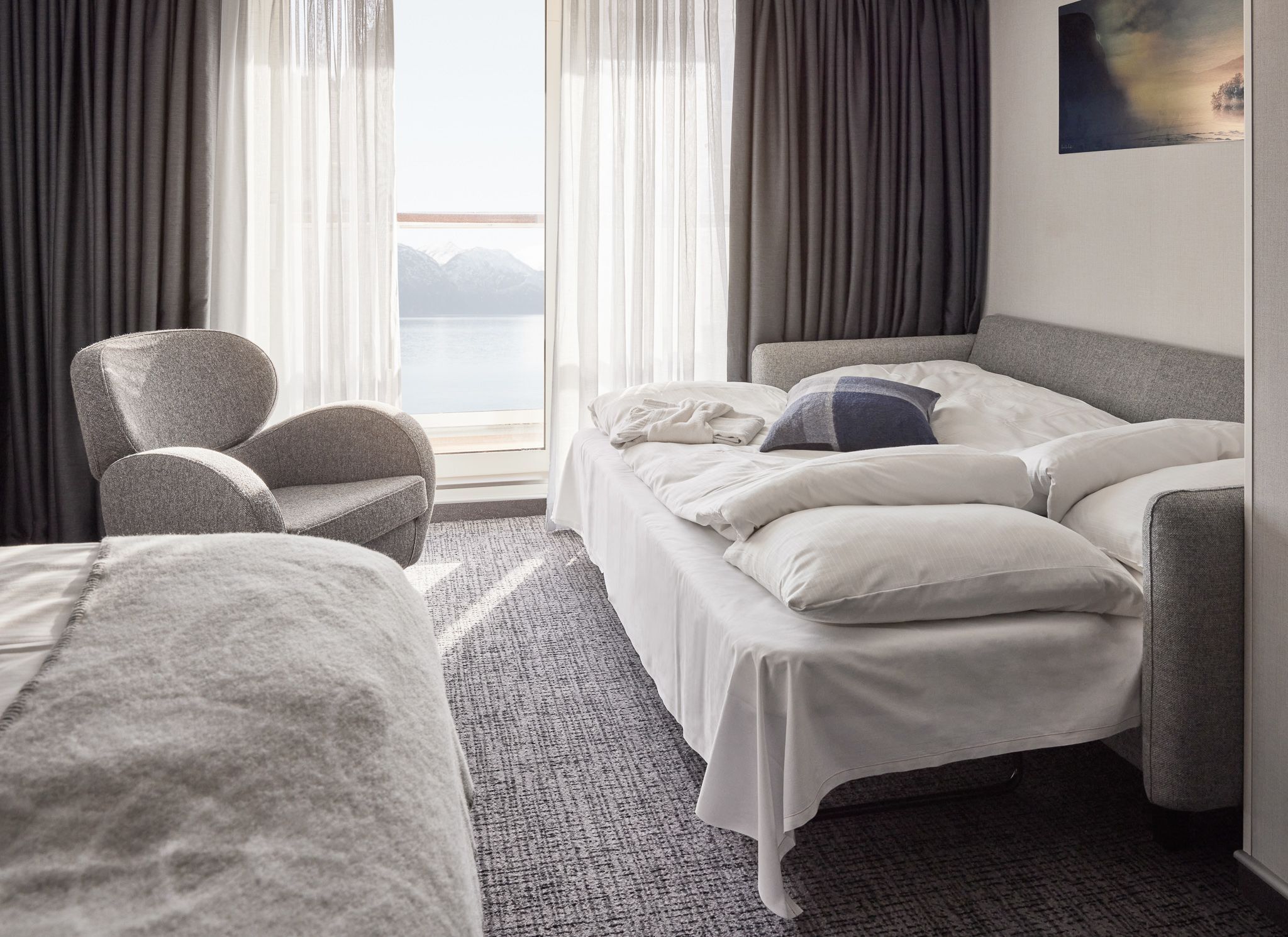 Balcony Junior Suite with the sofa bed unfolded into a bed, an armchair, floor-to-ceiling windows, and a private balcony with sea views.