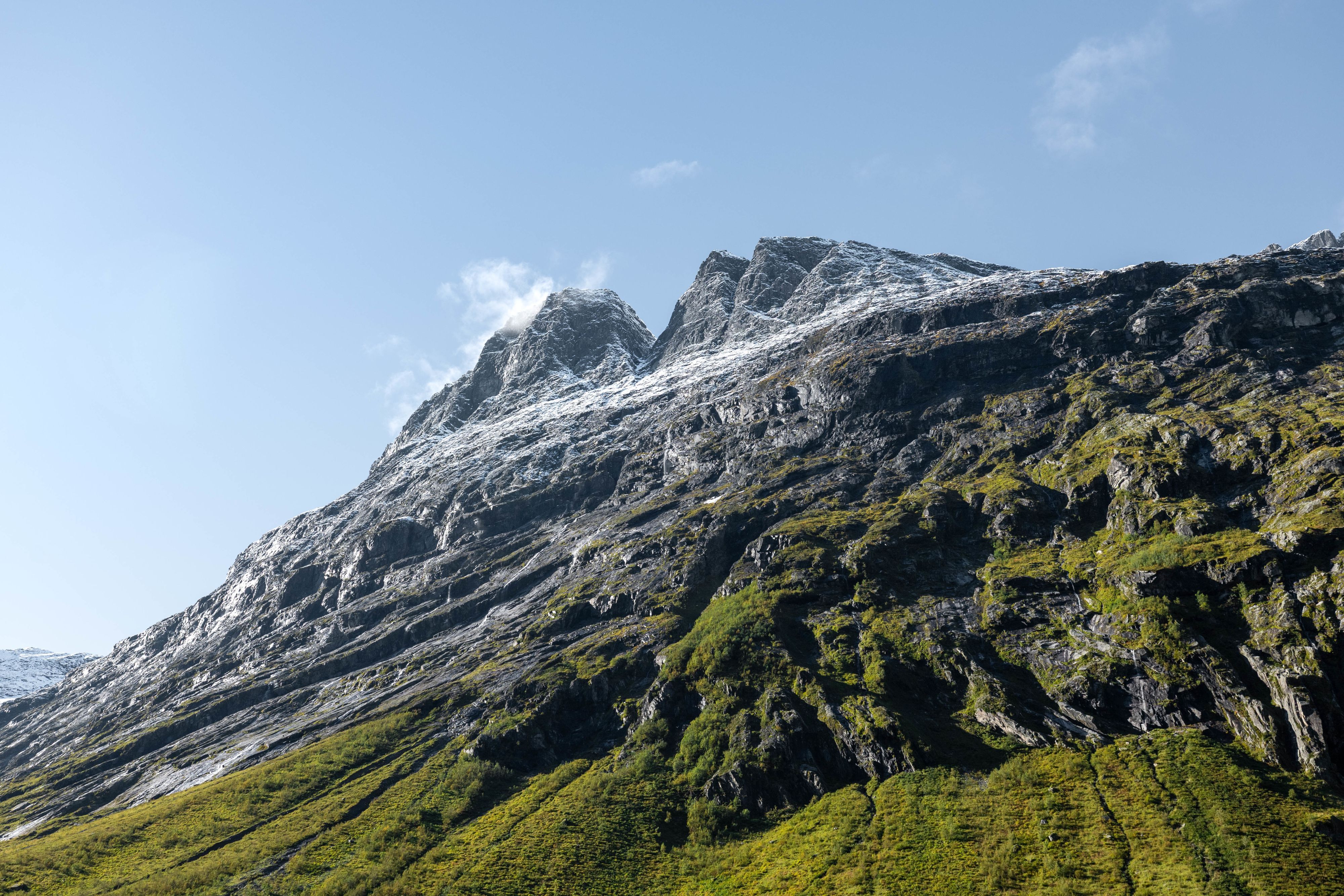 Rugged snow-dusted mountain peak with green slopes under a clear blue sky in rural Norway