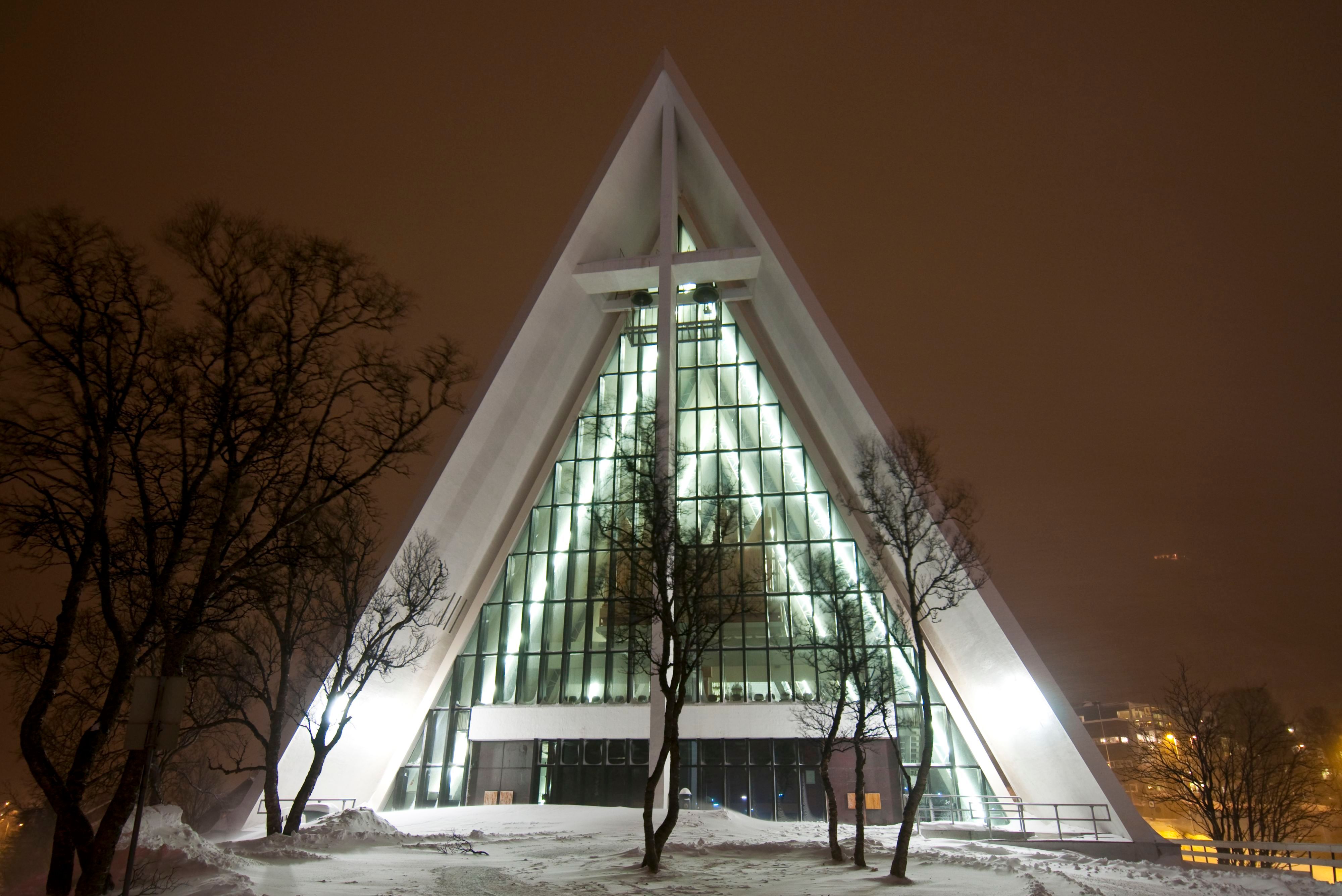Die Eismeerkathedrale (Ishavskatedralen), nachts beleuchtet in Tromsø, Norwegen, mit ihrer markanten dreieckigen Architektur, umgeben von einer verschneiten arktischen Landschaft