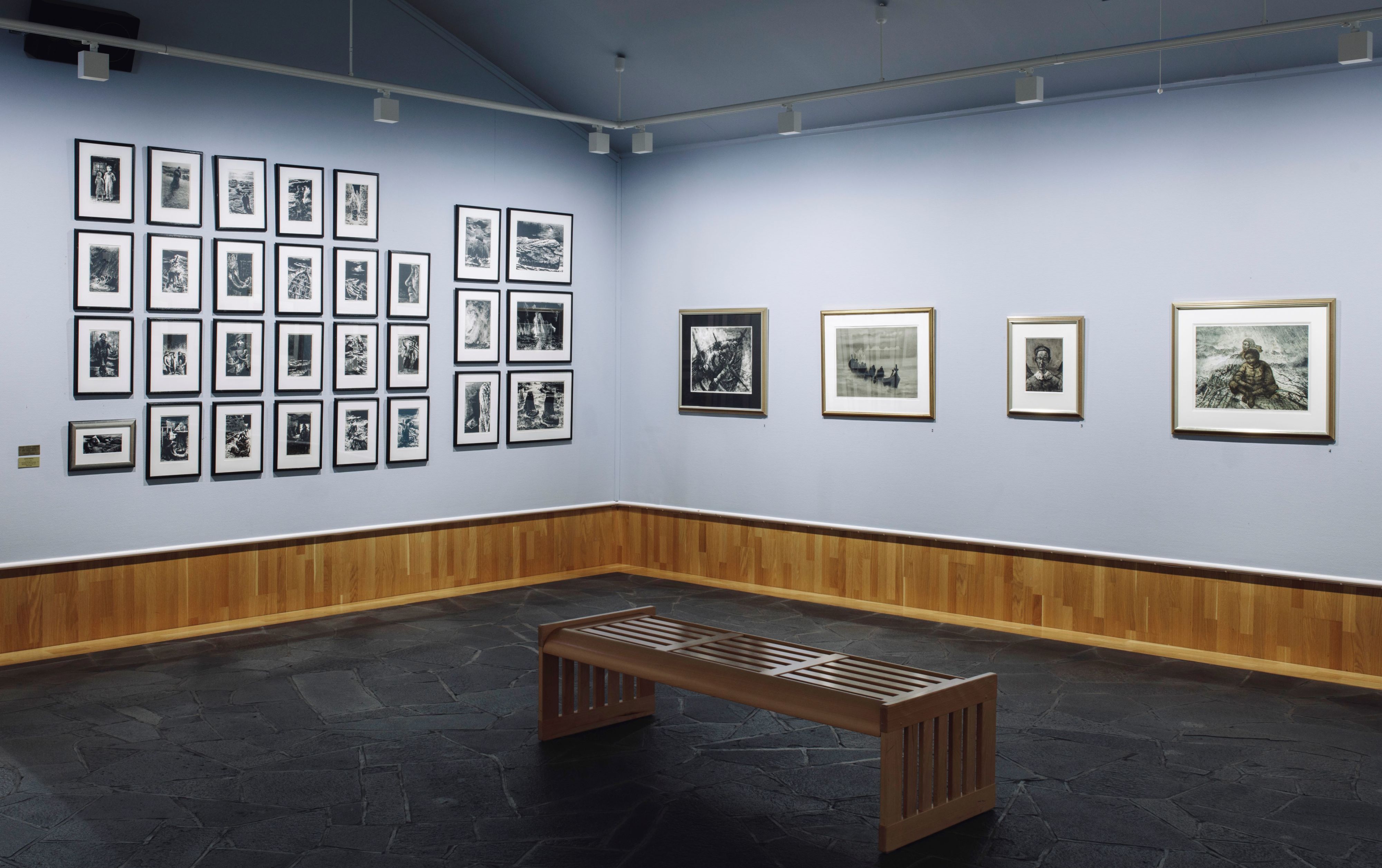 Interior of an art gallery with framed black-and-white artworks on blue walls and a wooden bench in Lofoten, Norway