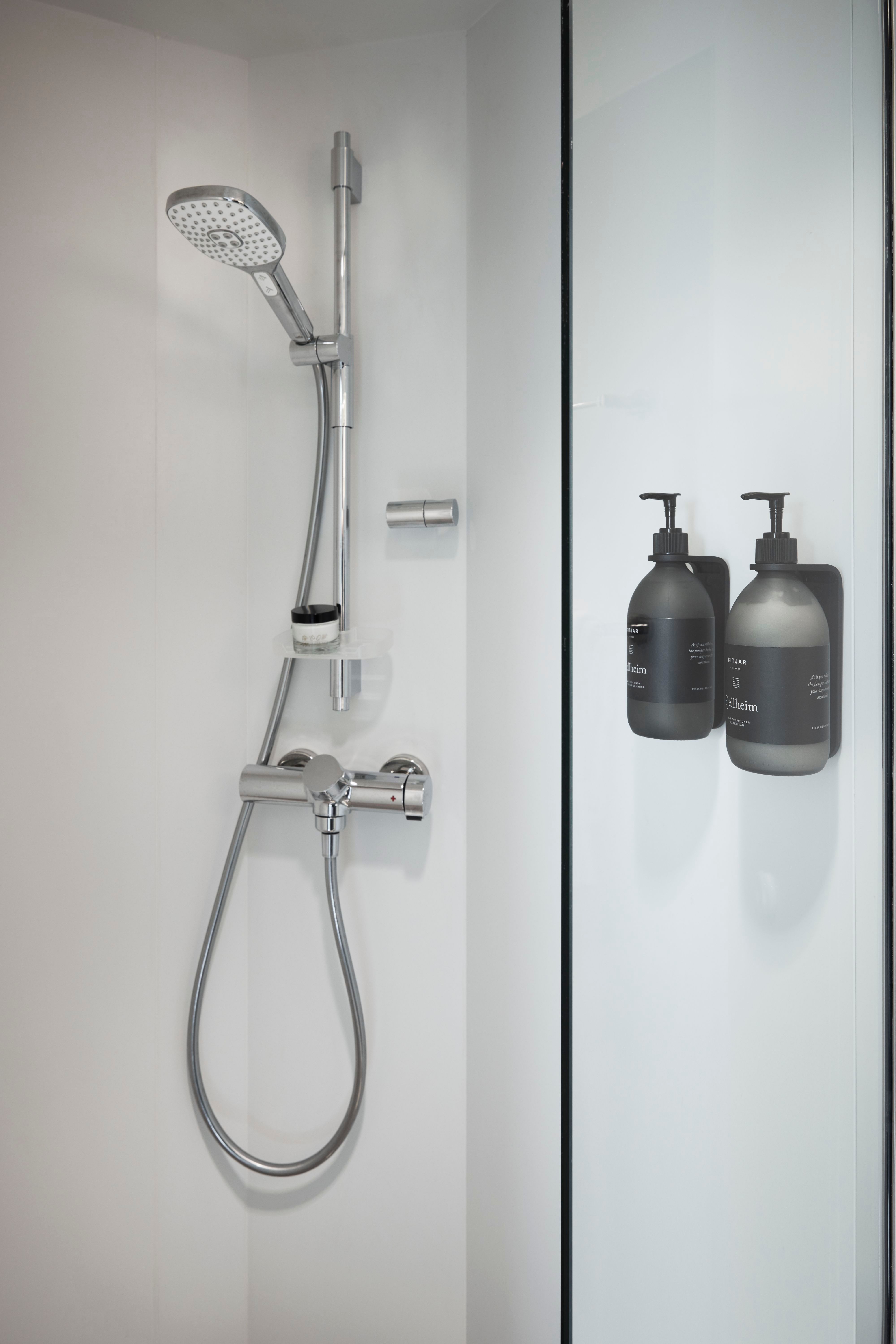 Walk-in shower with a handheld showerhead, glass partition, and wall-mounted shampoo and conditioner dispensers in a clean, modern design.