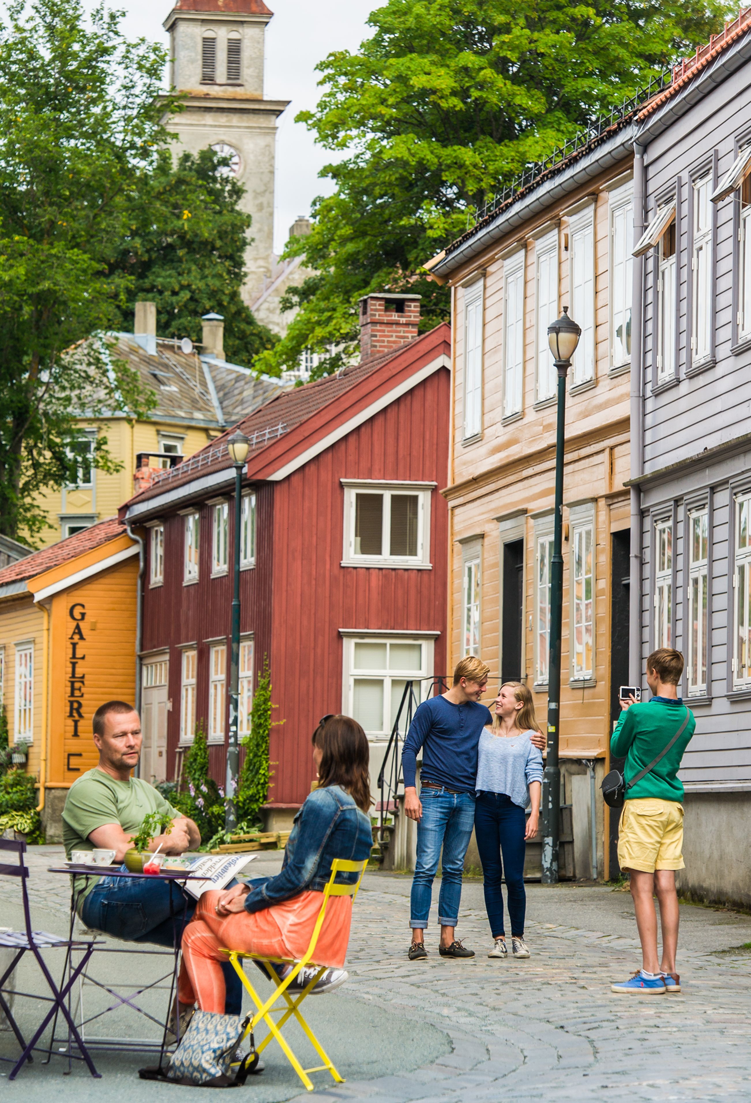 Menschen, die eine Kopfsteinpflasterstraße mit bunten Holzhäusern und einem Café im Stadtteil Bakklandet in Trondheim, Norwegen, genießen