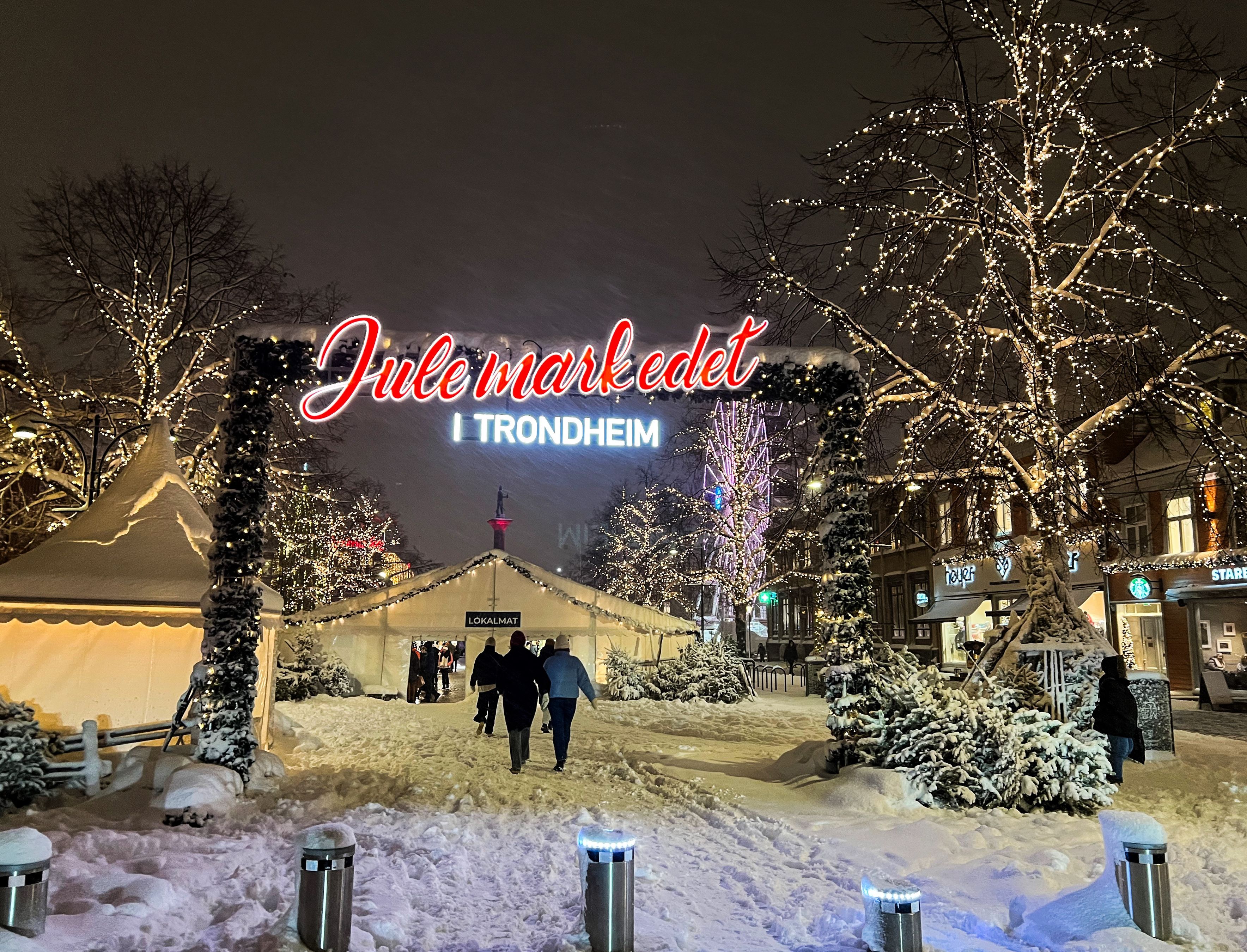 Illuminated Julemarkedet entrance sign and snowy market stalls at the Trondheim Christmas market at night, Norway