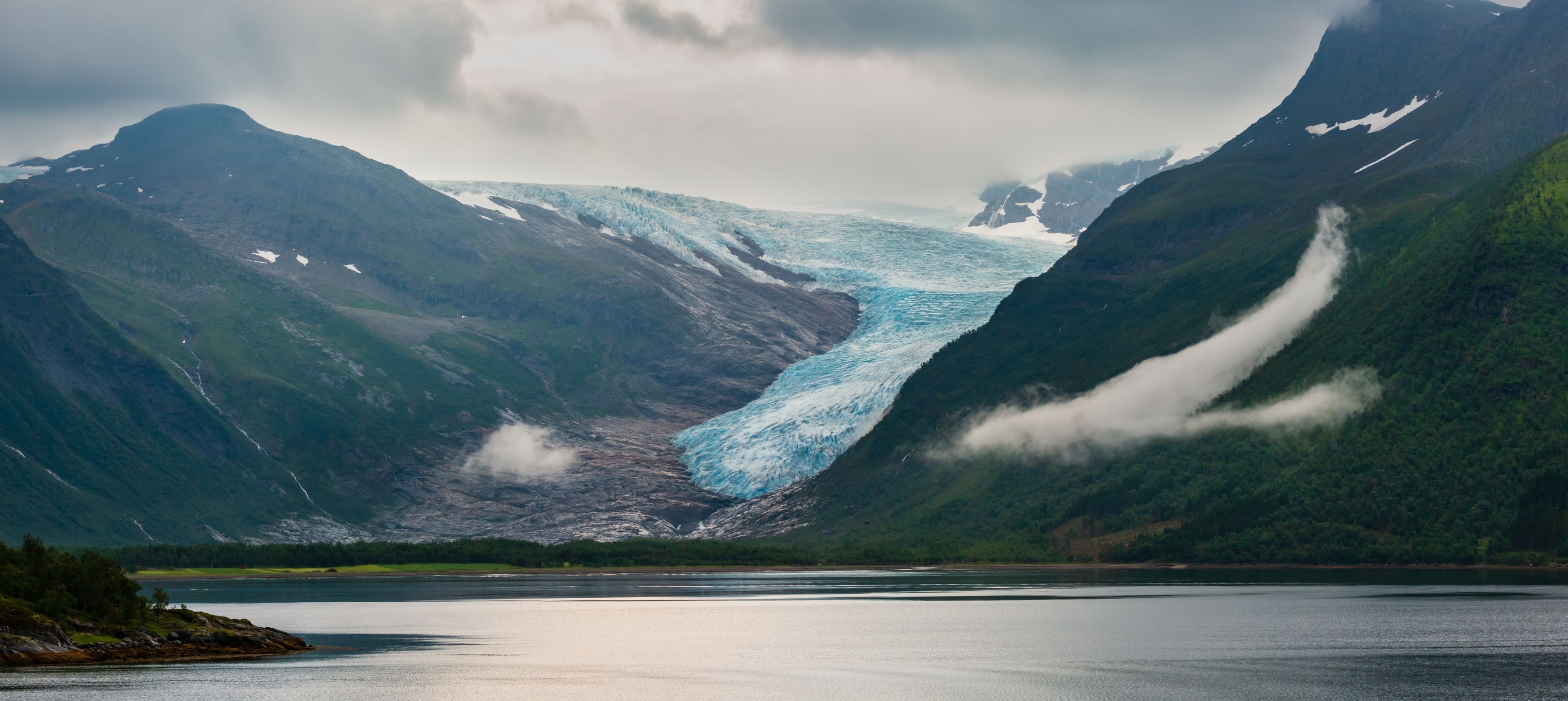 Panoramablick auf einen majestätischen norwegischen Gletscher, der sich durch ein Bergtal über einem friedlichen Fjord erstreckt