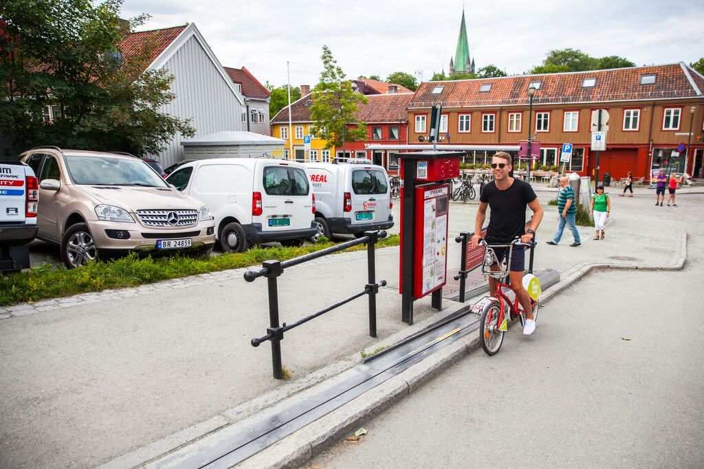 Radfahrer nutzt den Trampe-Fahrradlift in einer Straße mit dem Kirchturm des Doms in Trondheim, Norwegen