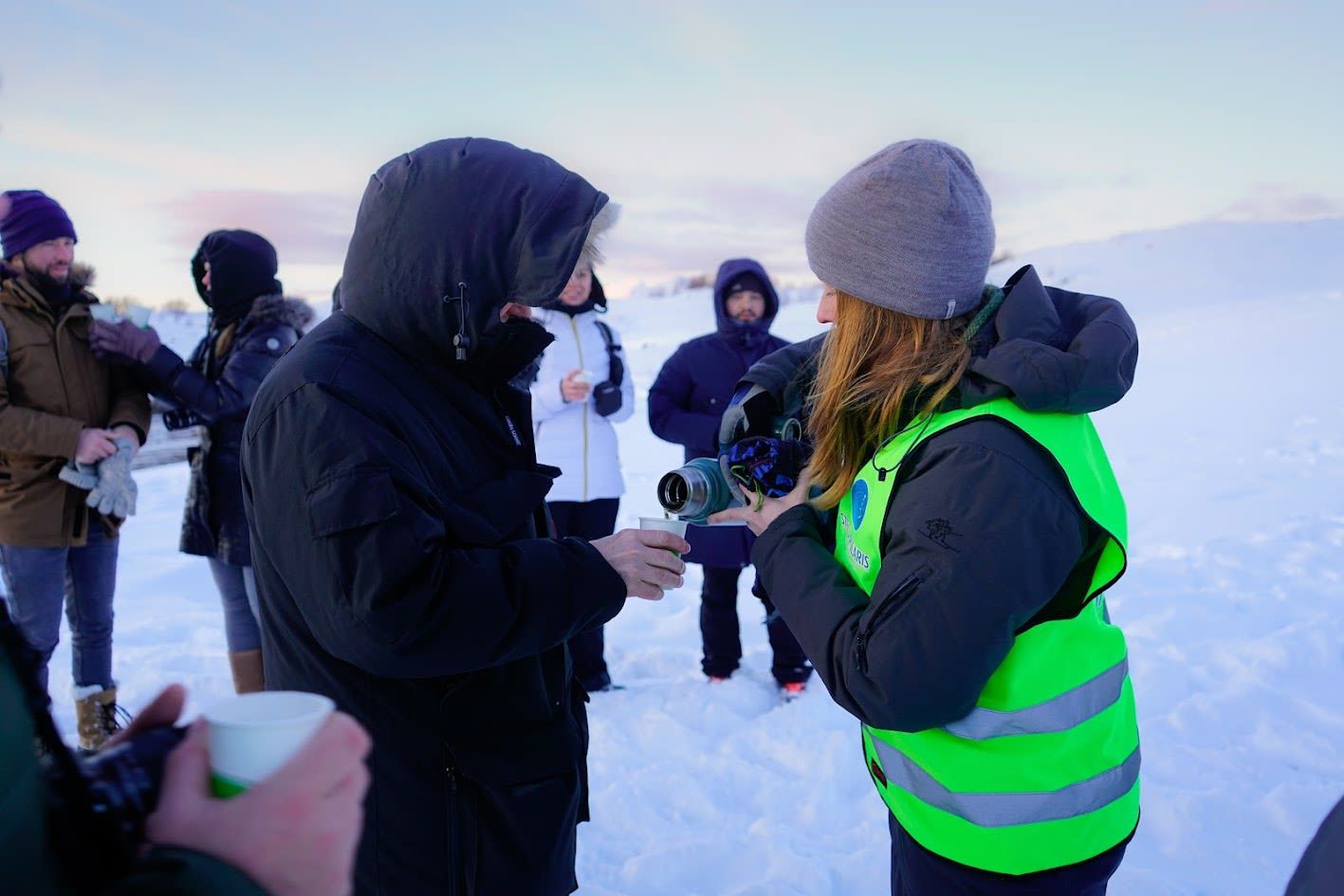 Guide som skjenker en varm drikke til besøkende under en pause på en snødekt vintertur i Arktis i Norge