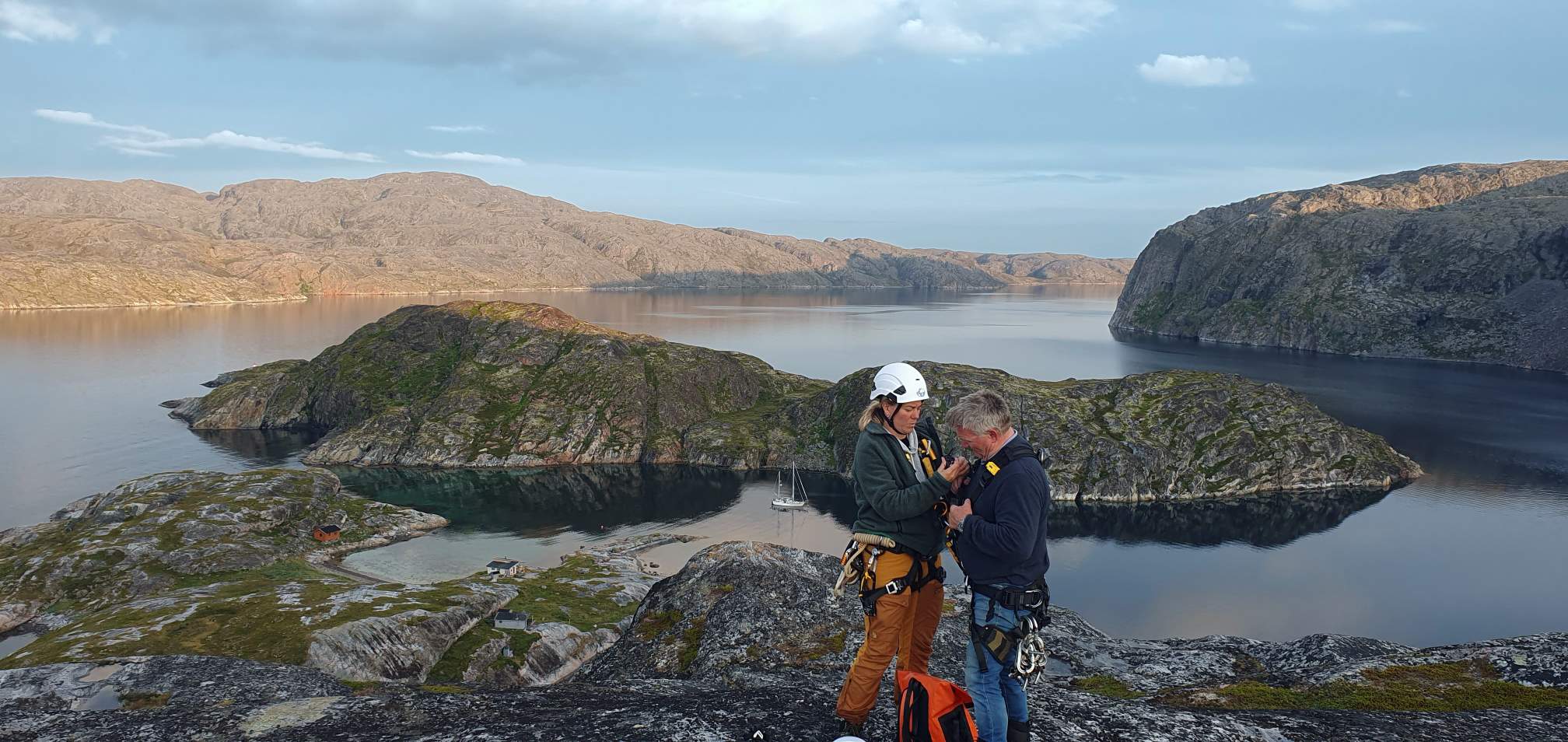 Guide assisting a participant with climbing equipment before the Arctic Rappelling Route, overlooking a scenic Arctic fjord in Northern Norway.