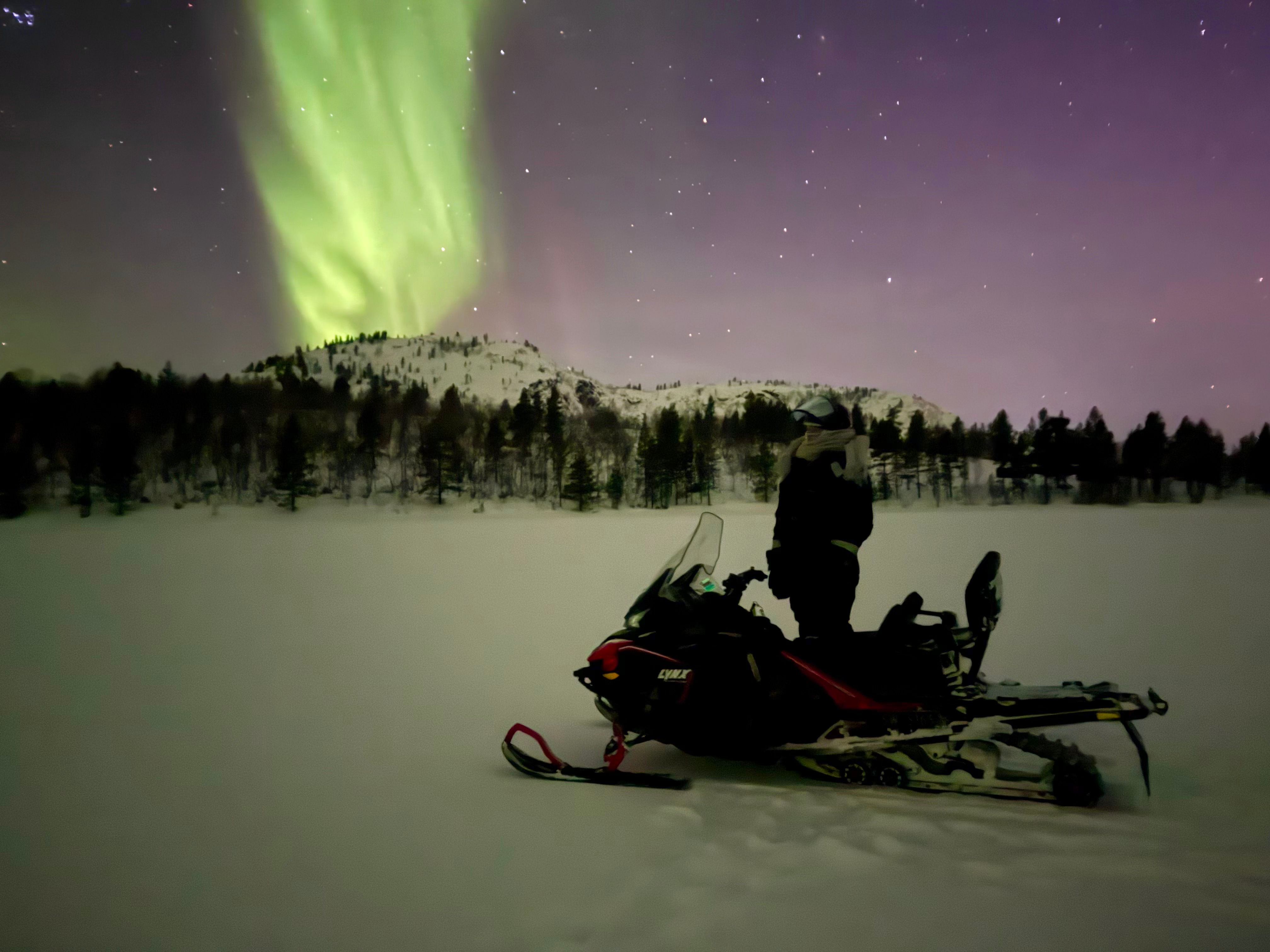 Snöskoterförare som tittar upp på norrskenet