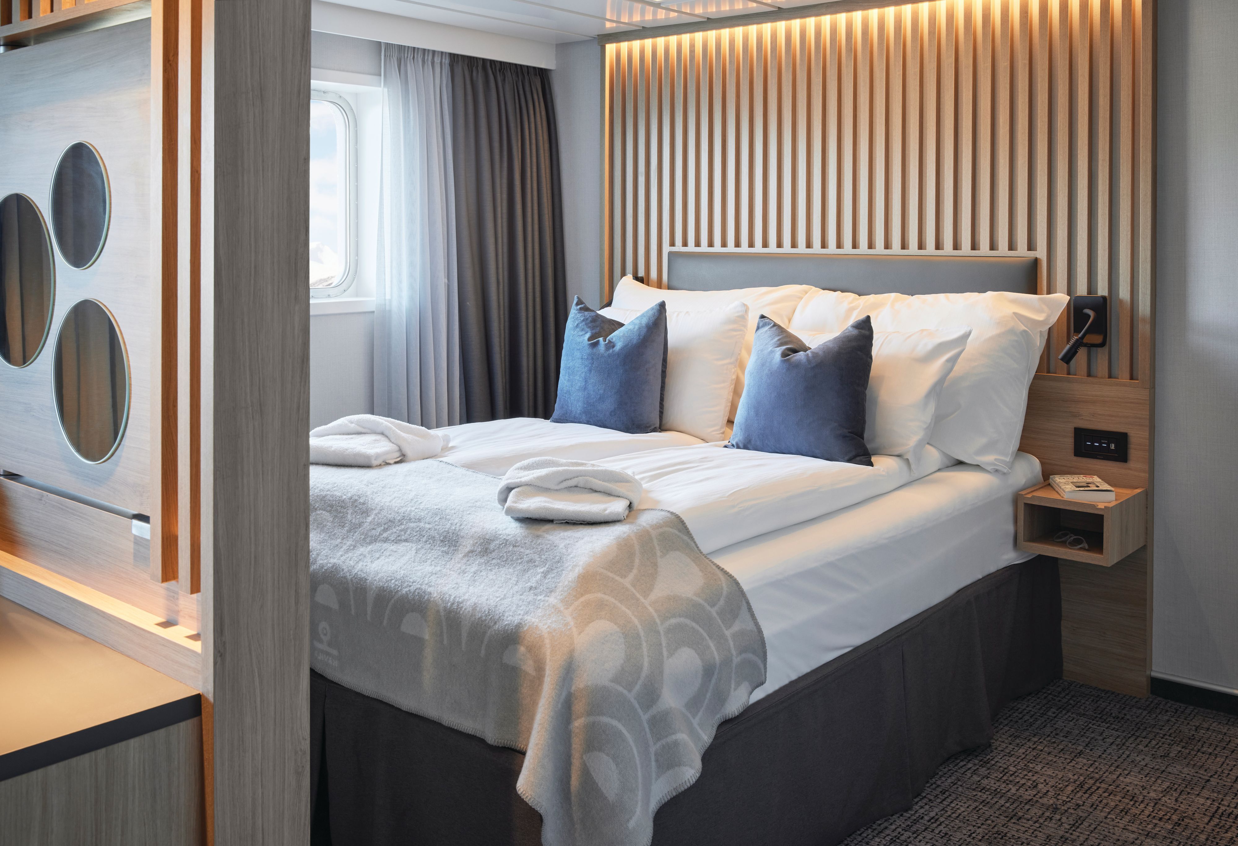 Soverom i Seaview Junior Suite med king-size-seng med førsteklasses sengetøy, dekorativ sengegavl i tre, leselys, roterende TV-vegg og et vindu som fyller suiten med naturlig lys.