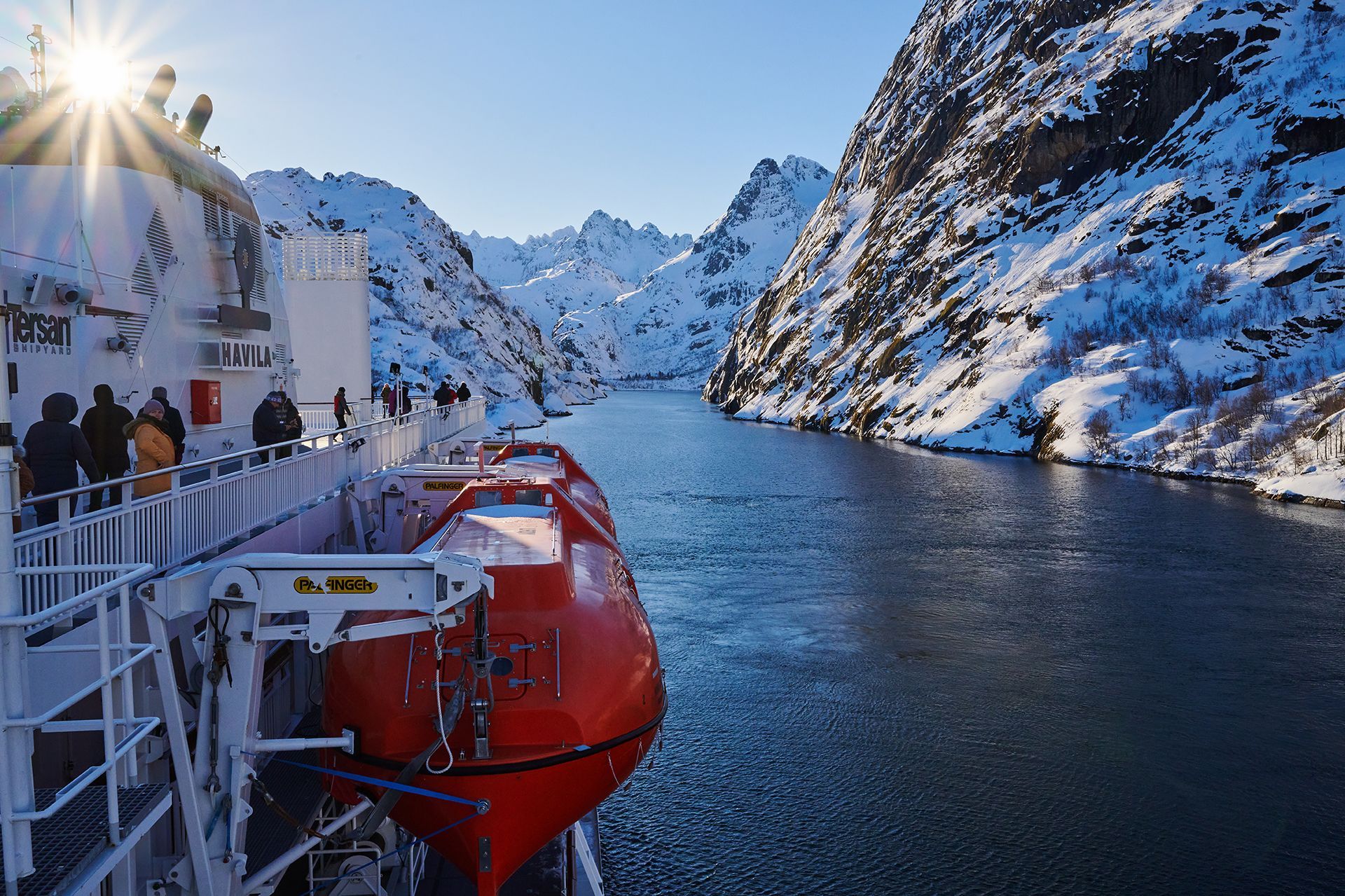 Guests on deck as the ship sails through the narrow, snow-covered Trollfjord