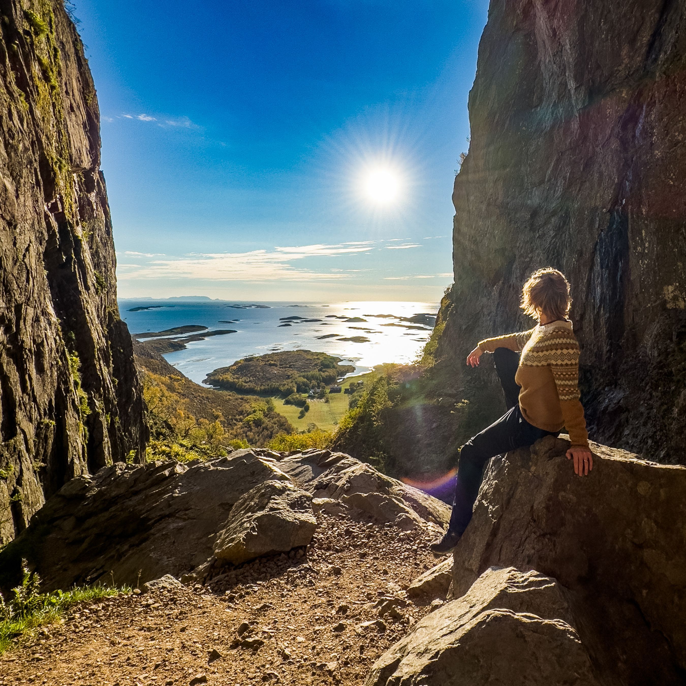 Visitor walking along a coastal walkway overlooking the Norwegian Sea at sunset.