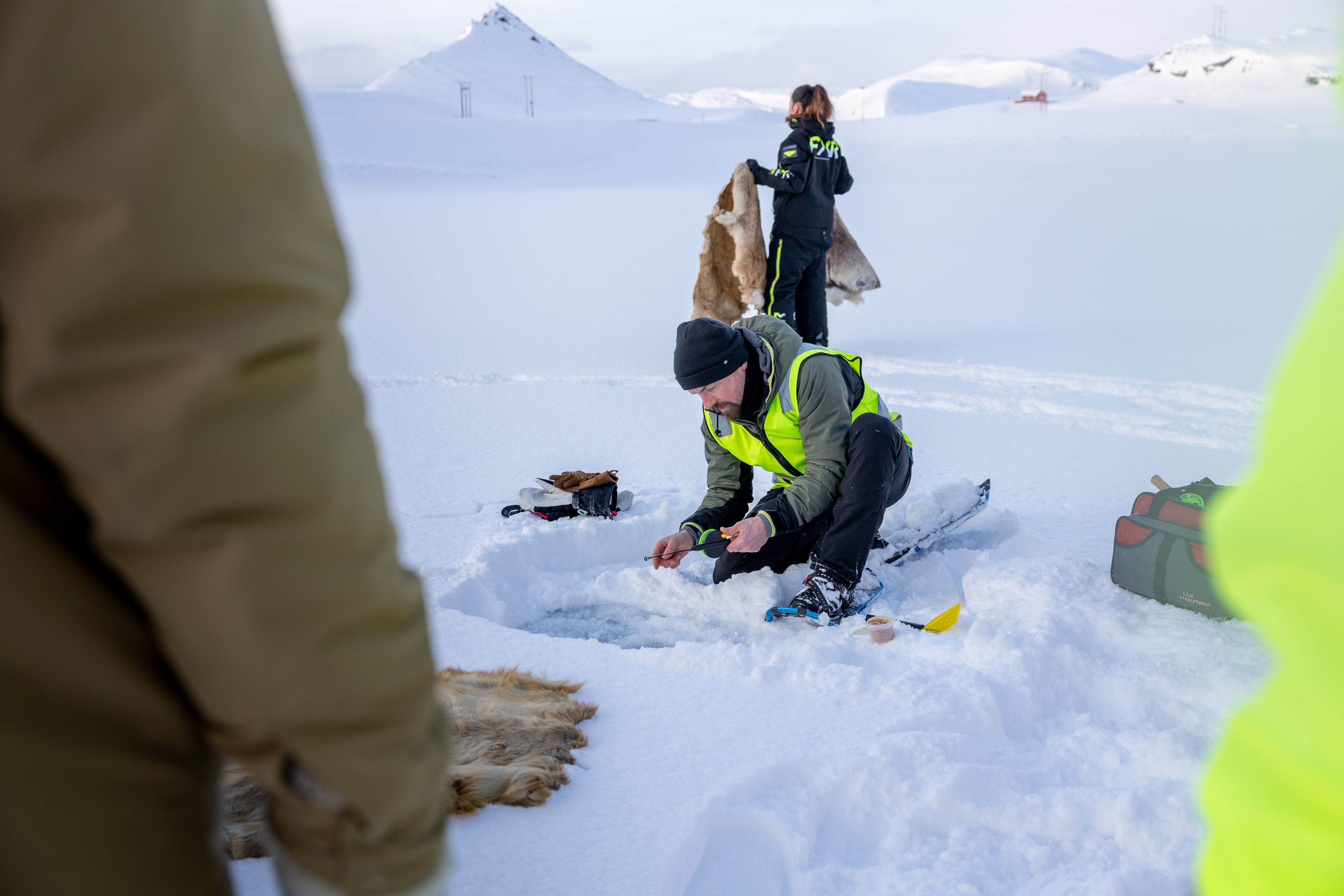 Guide preparing ice fishing gear during a snowshoeing tour in Arctic Honningsvåg.