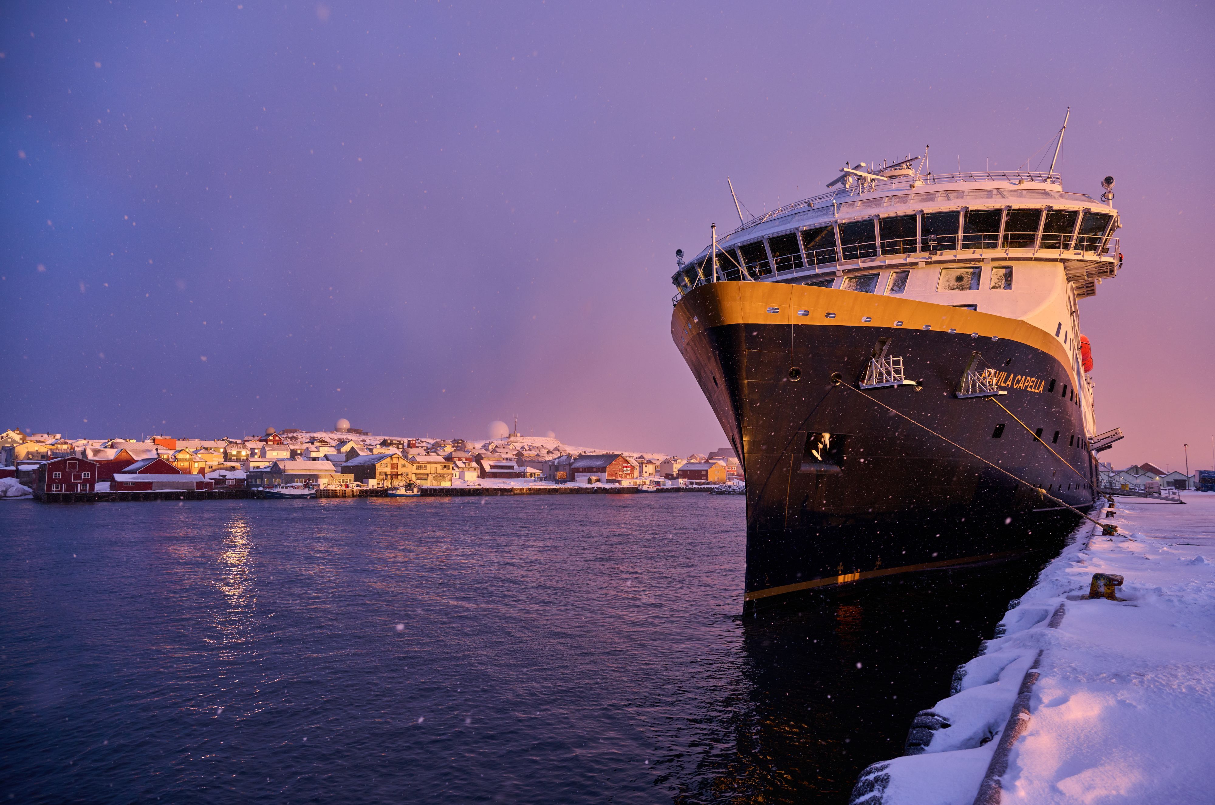 Havila Capella docked along the snowy Norwegian coast during a calm winter evening.