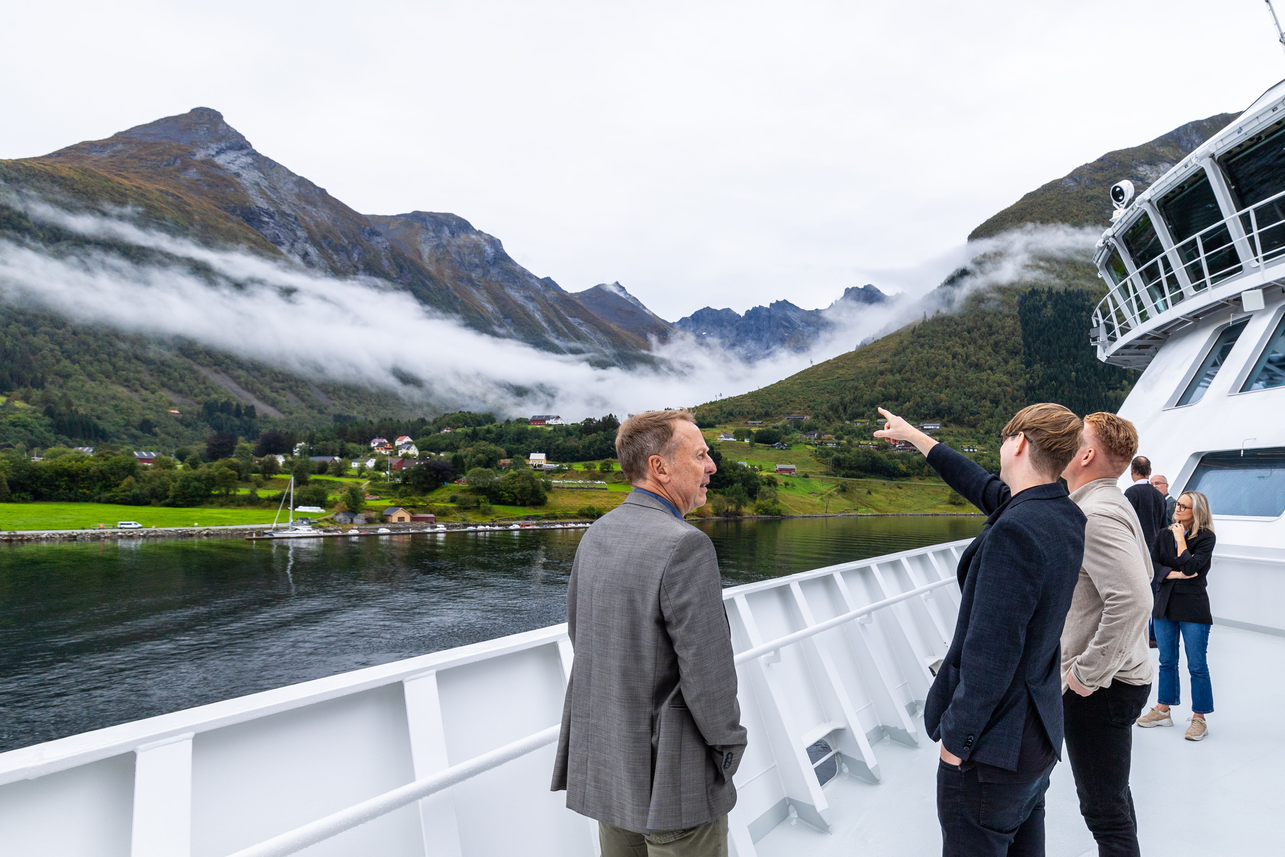 Gäster på däck ser låga moln svepa över de gröna bergssluttningarna längs fjorden