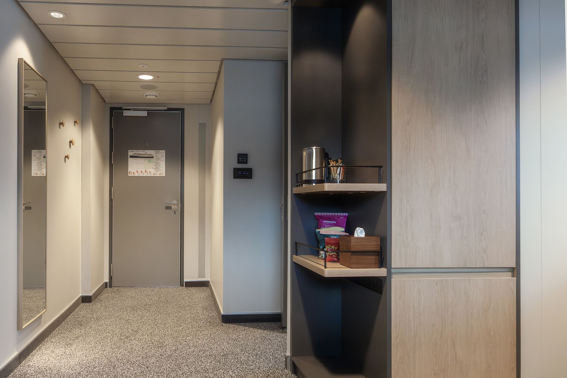 Eingangsbereich der Aft View Mini Suite mit einem Ganzkörperspiegel, einem Kleiderschrank, offenen Regalen mit Kaffeestation und Erfrischungen sowie einem großzügigen Flur, der in die Suite führt.