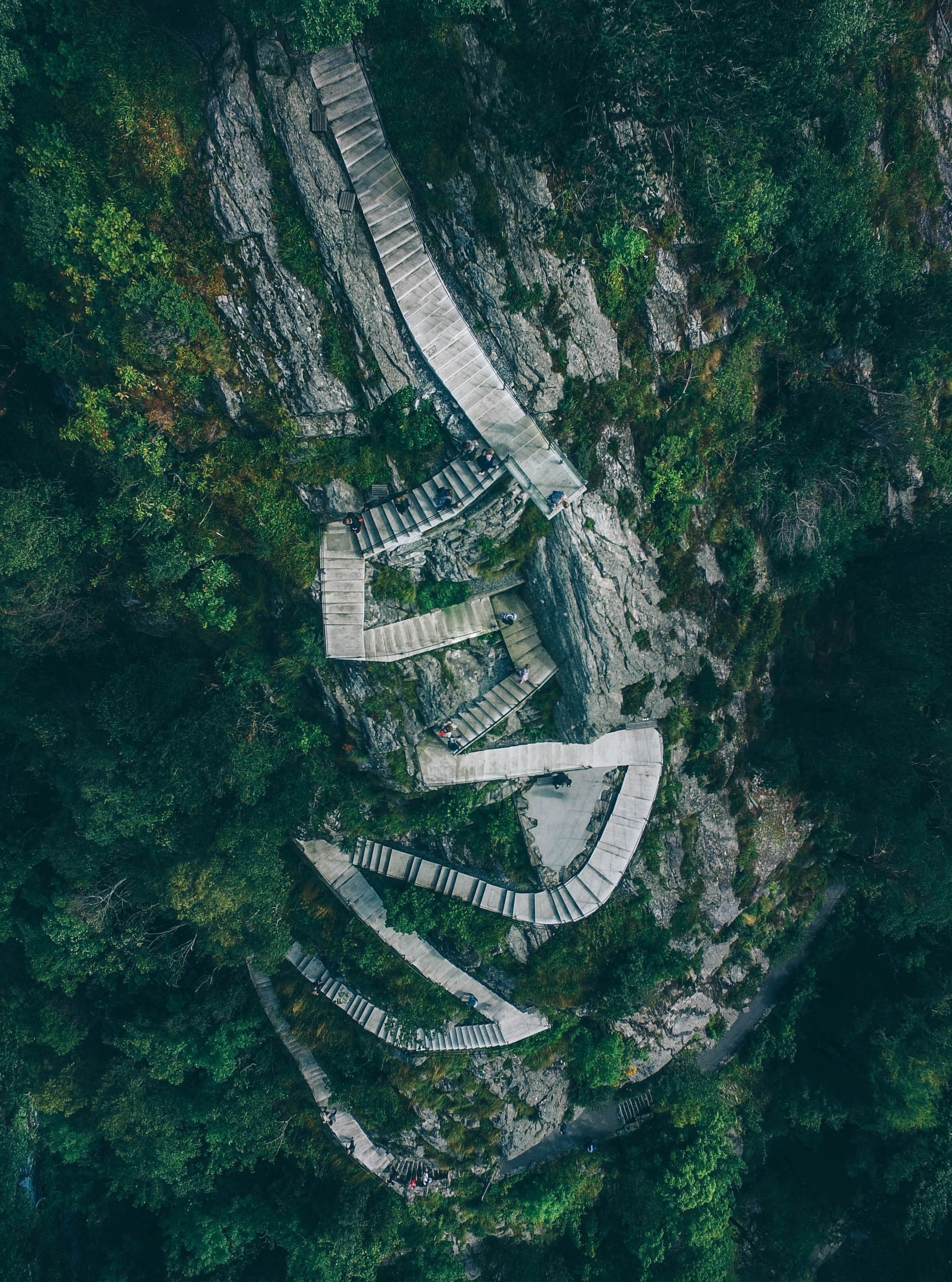 Luftaufnahme der berühmten Aksla-Treppe in Ålesund, die sich durch einen üppig grünen Wald und felsige Klippen windet, während Besucher den malerischen Weg hinaufsteigen.