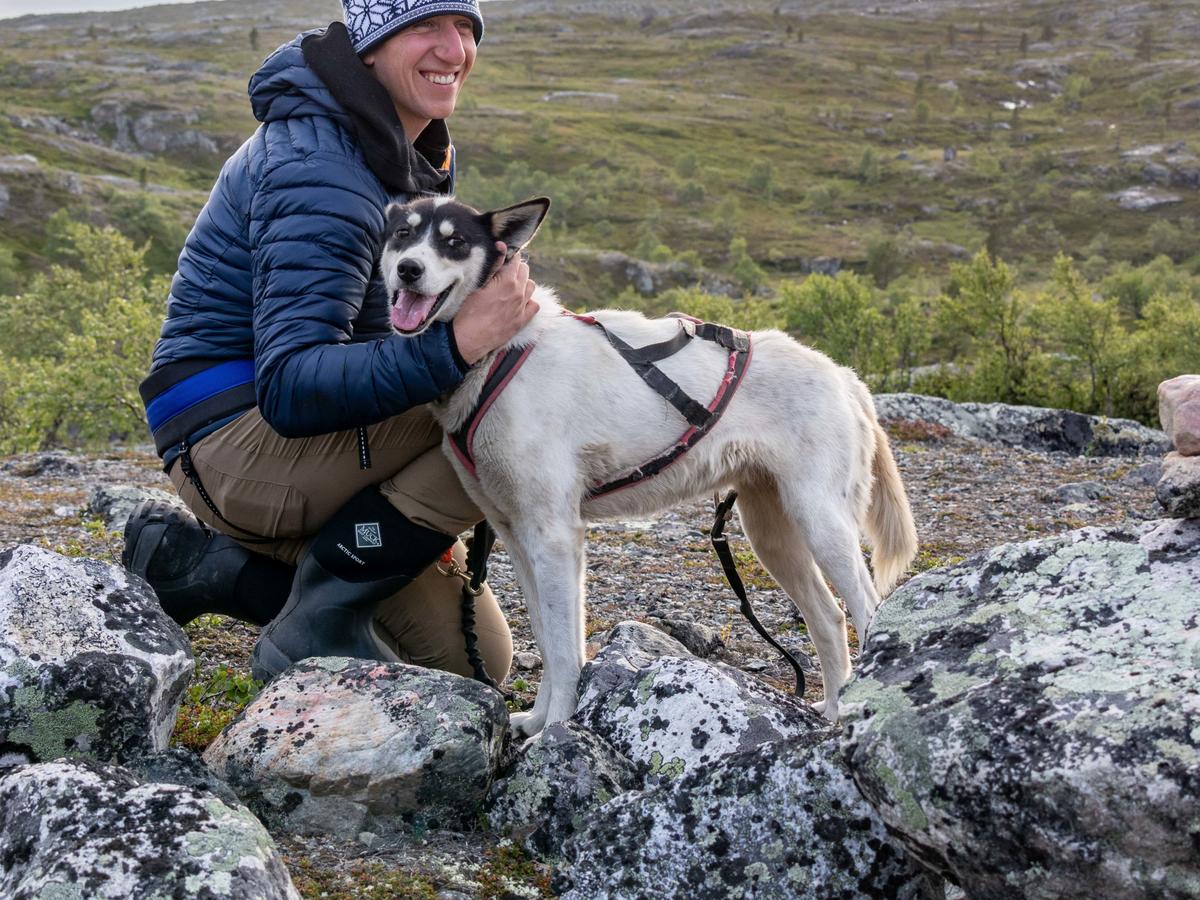 Hiker with a harnessed husky on rocky terrain in the Arctic landscape near Kirkenes.
