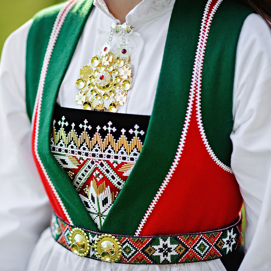 Close-up of a traditional Norwegian bunad folk costume with green and red embroidery, beadwork, and a silver brooch in May, Norway
