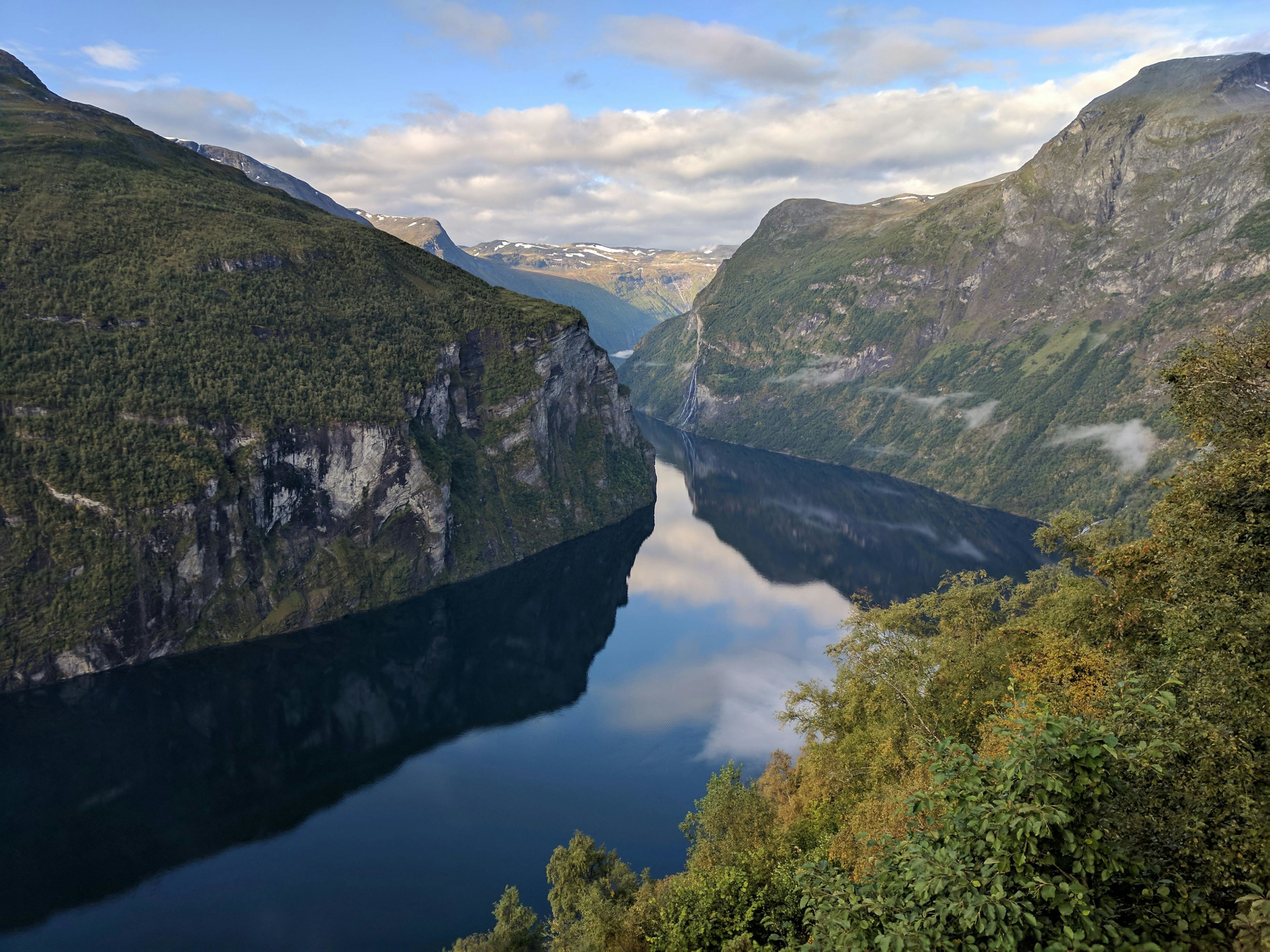 Havila-cruiseskip som seiler gjennom Geirangerfjorden, omgitt av ruvende fjell og krystallklart vann om sommeren.