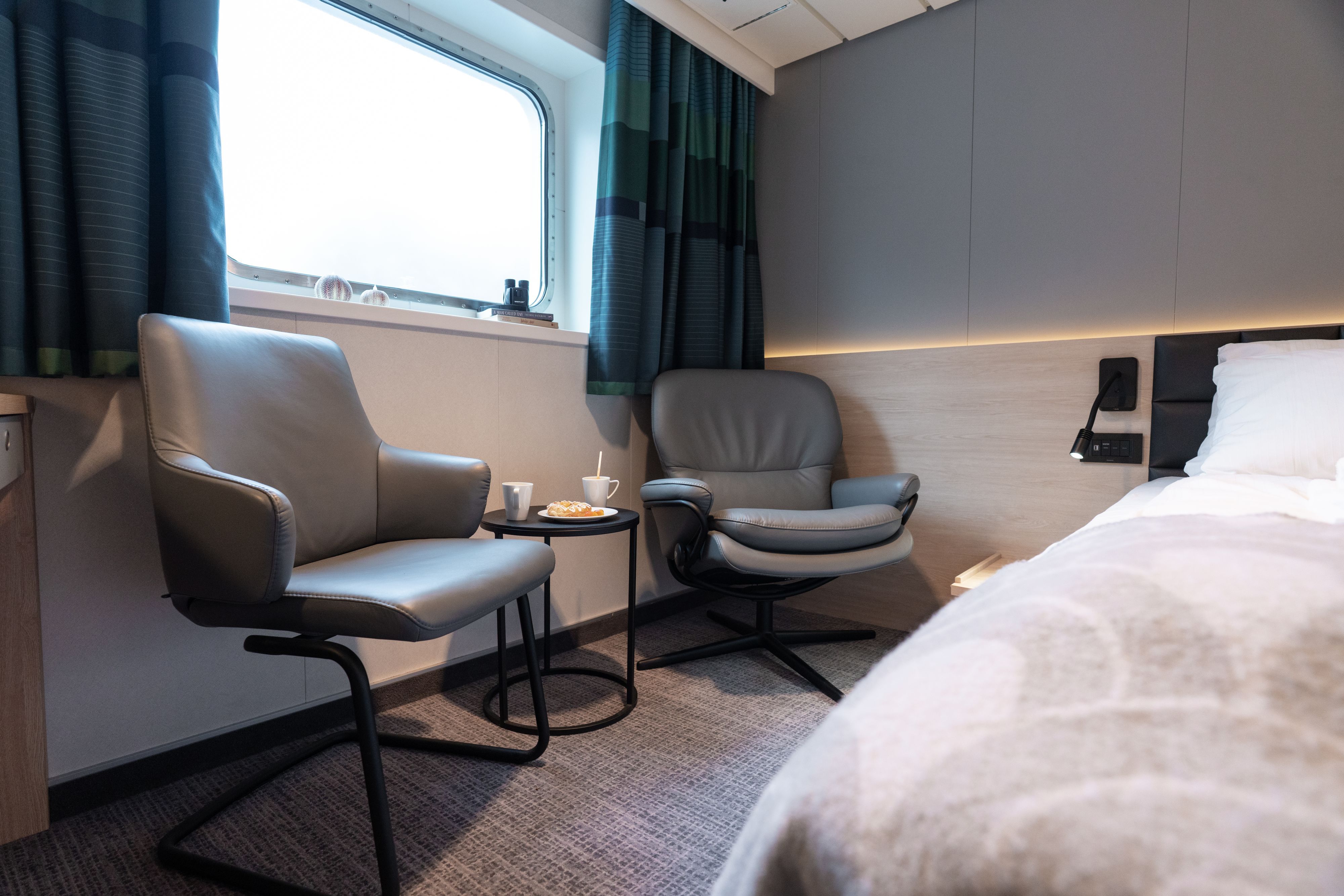 Seaview Superior King Kreuzfahrtkabine mit Sitzecke, Lounge-Sesseln, Beistelltisch, großem Fenster und entspannendem Meerblick.