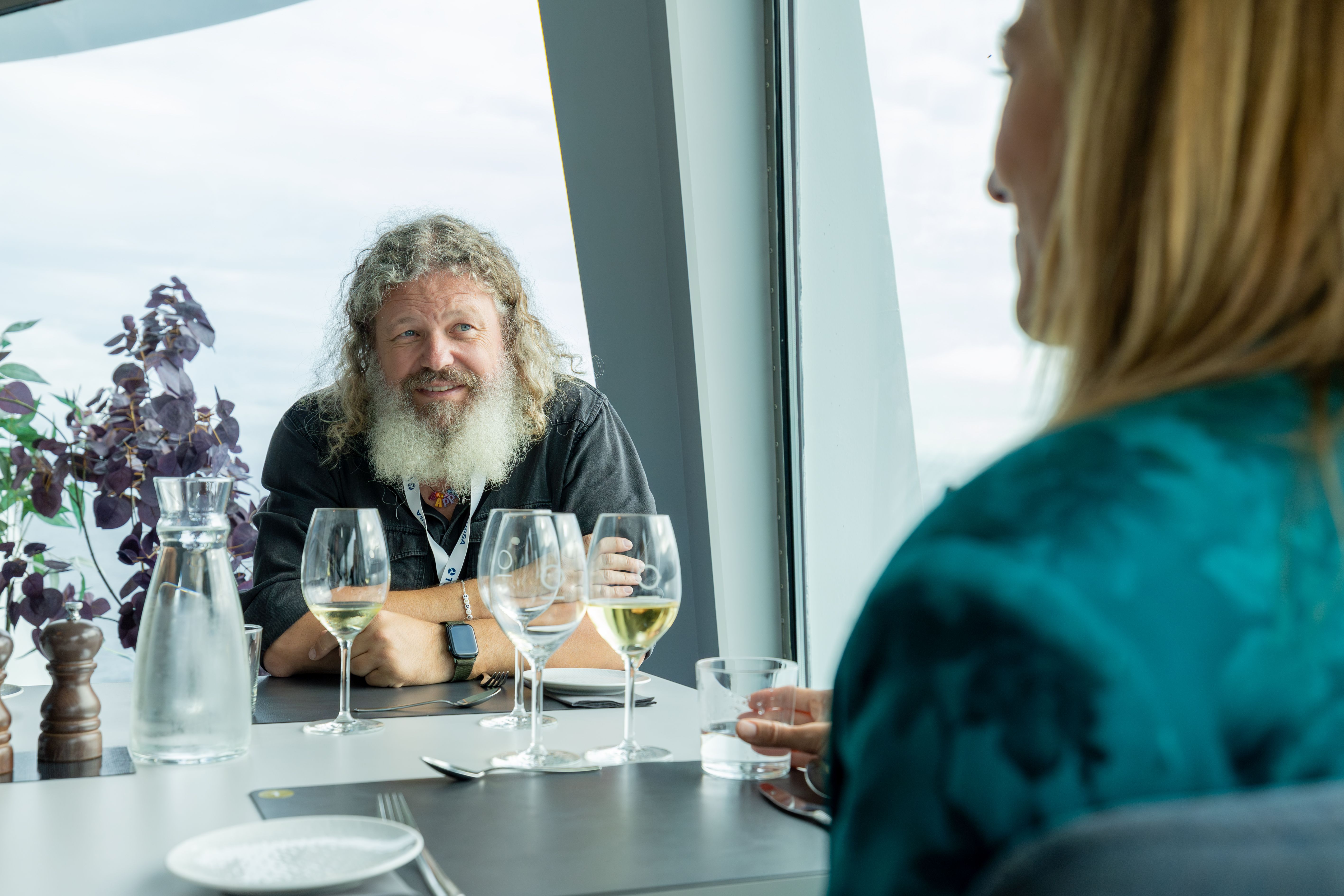 To gjester snakker sammen over hvert sitt glass hvitvin ved et vindusbord om bord
