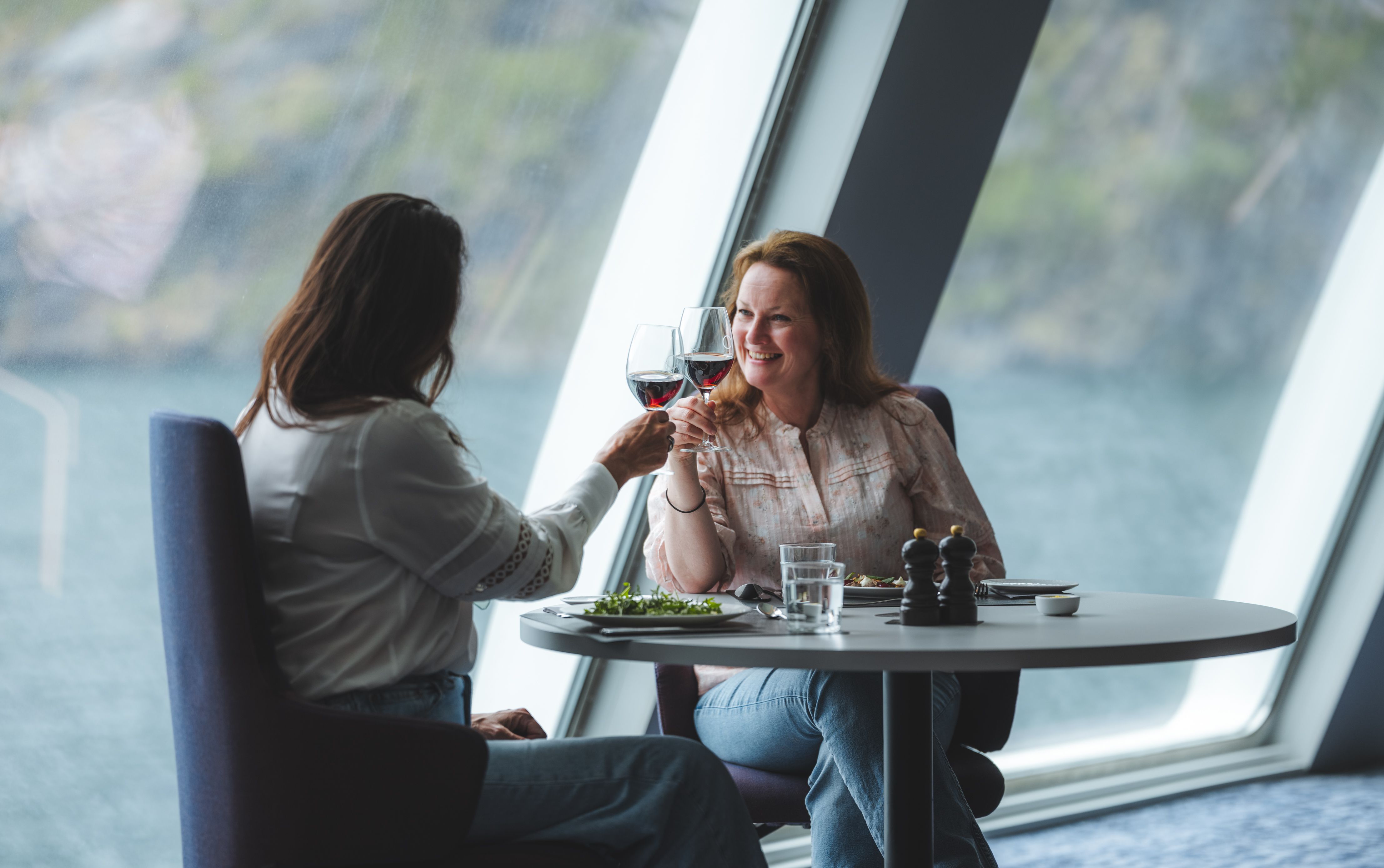 To gjester skåler med rødvin ved et vindusbord med utsikt over fjorden