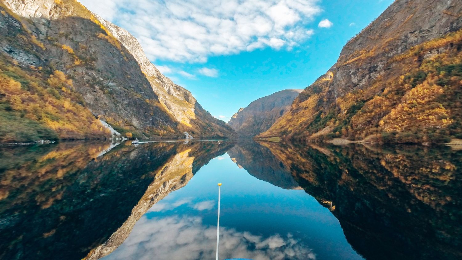 Spiegelglatte Reflexionen auf dem ruhigen Wasser des Nærøyfjords, umgeben von herbstlich gefärbten Bergen unter einem strahlend blauen Himmel in Westnorwegen.