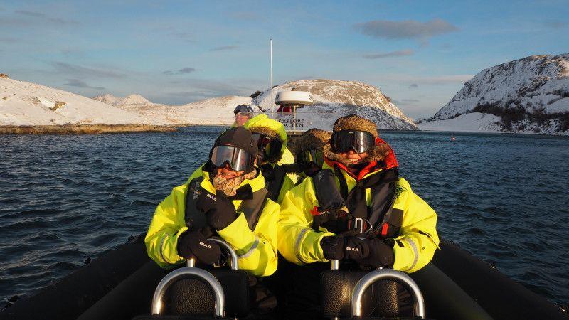 Gjester i isolerte flytedrakter nyter en RIB-tur i høy fart gjennom en snødekt arktisk fjord nær Bodø, omgitt av dramatiske vinterfjell og klart kystvann.