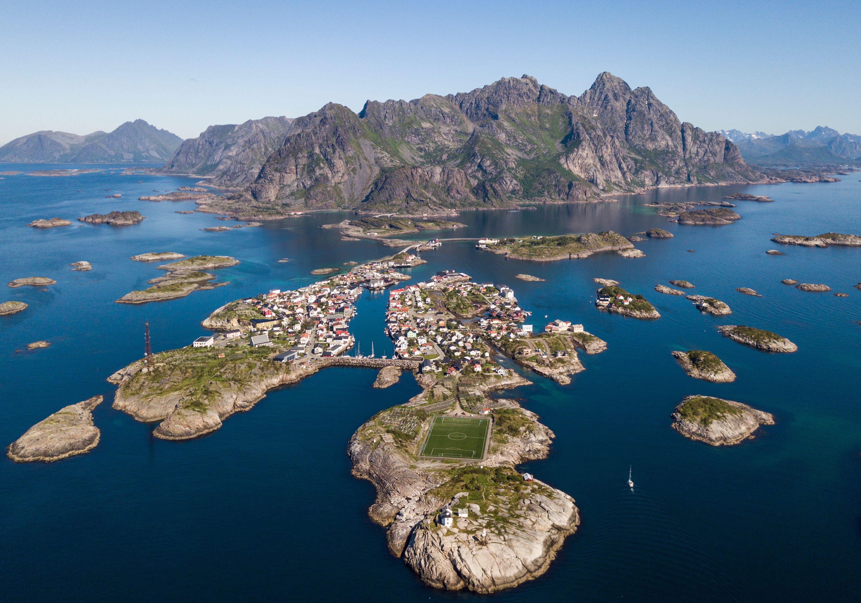 Luftaufnahme des Fischerdorfs Henningsvær, umgeben von Bergen und dem Norwegischen Meer in den Lofoten, Norwegen.