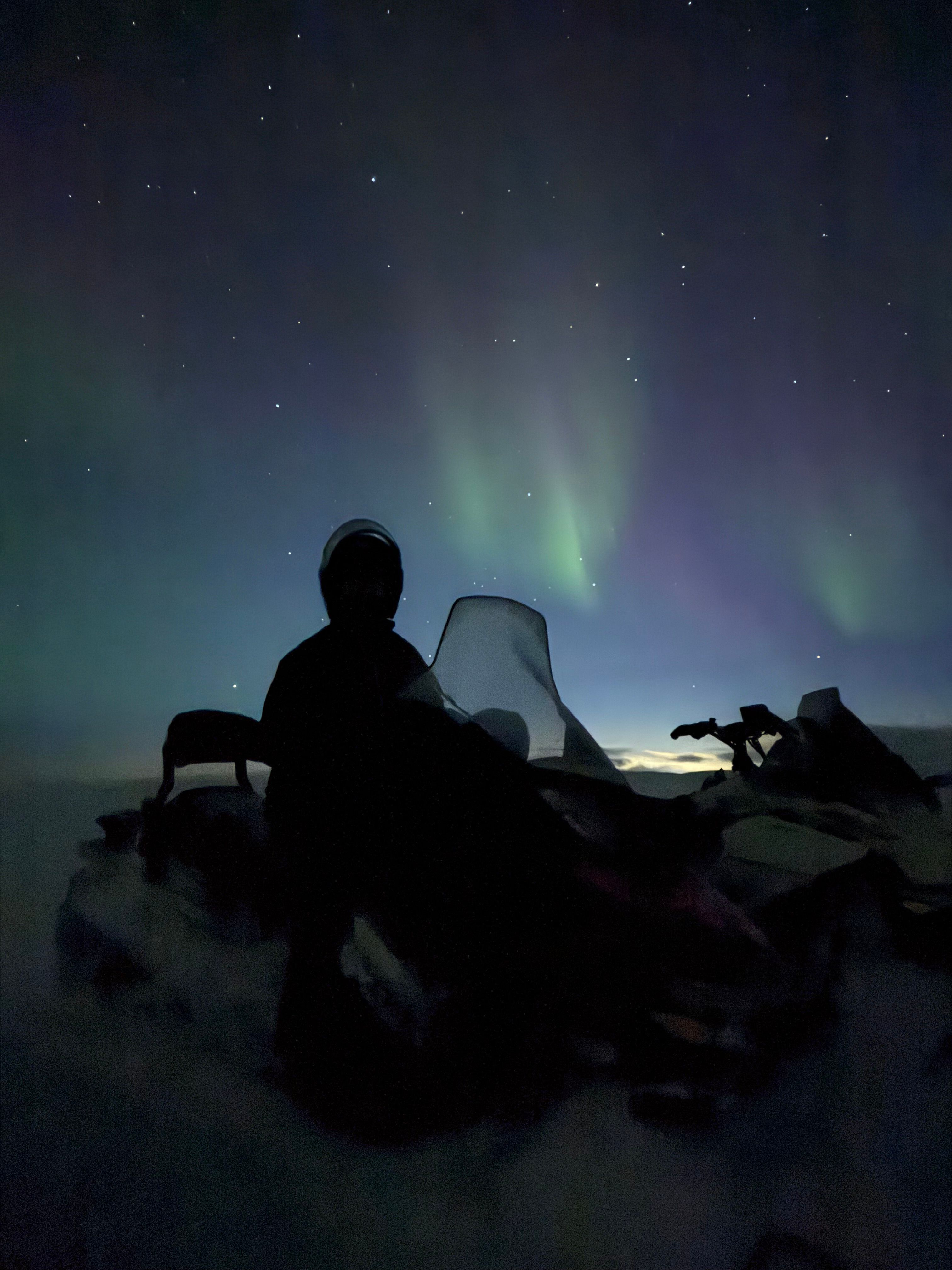 Snow mobile rider looking up at the northern lights