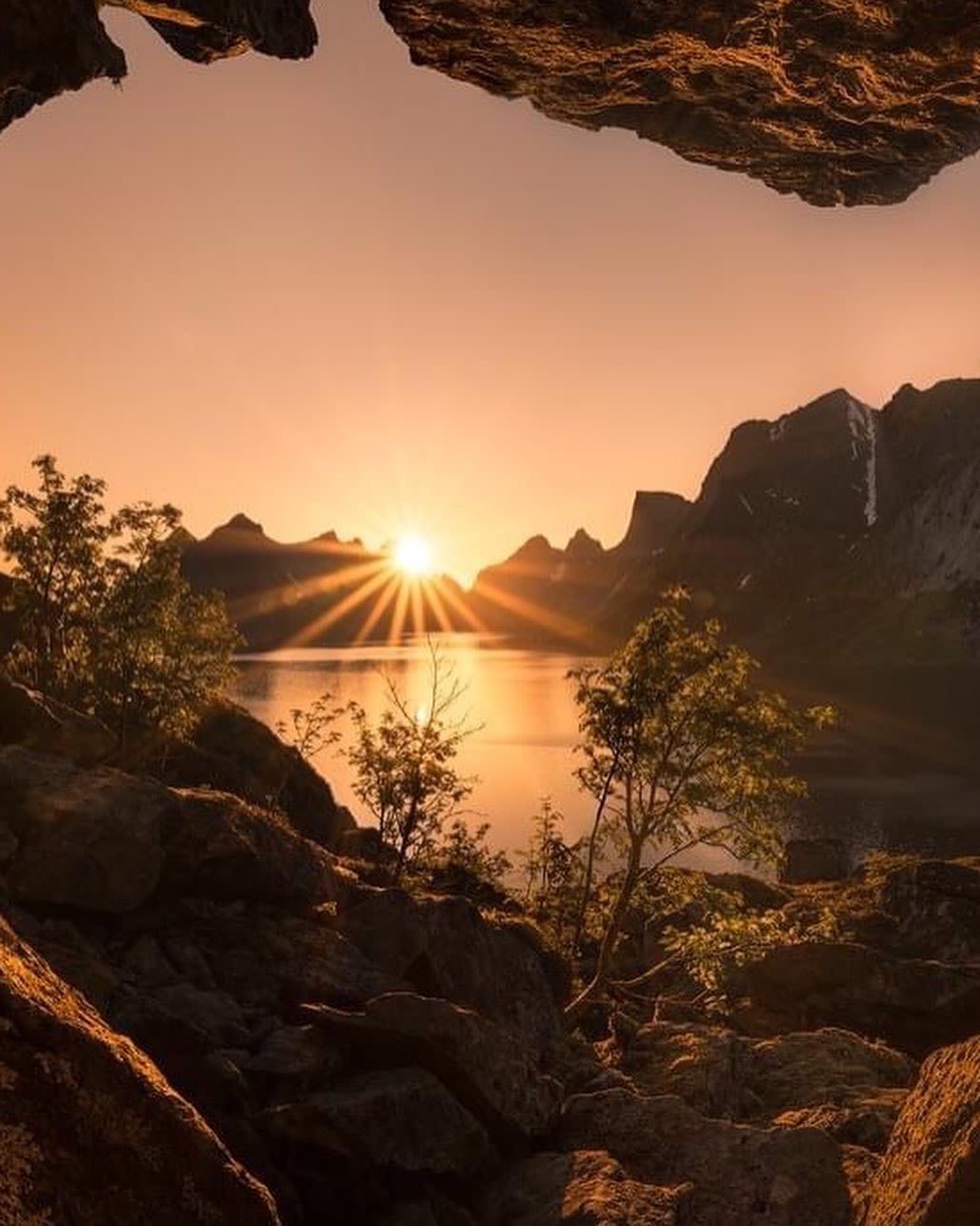Midnight sun over a tranquil fjord in the Lofoten Islands, Norway, framed by rugged mountains, rocky cliffs, and golden Arctic light