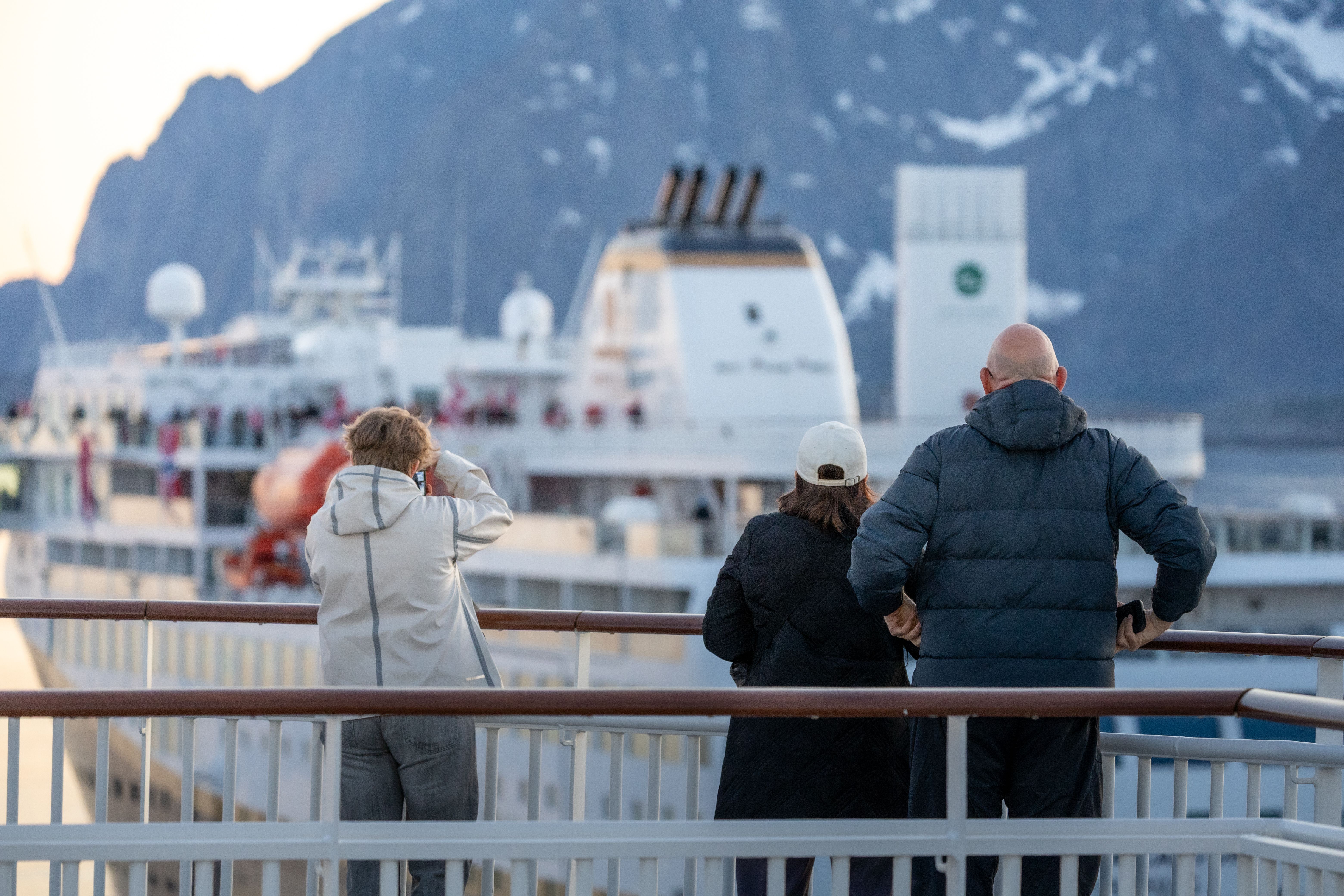 Tre gäster vid relingen som ser ett annat fartyg passera nedanför branta berg