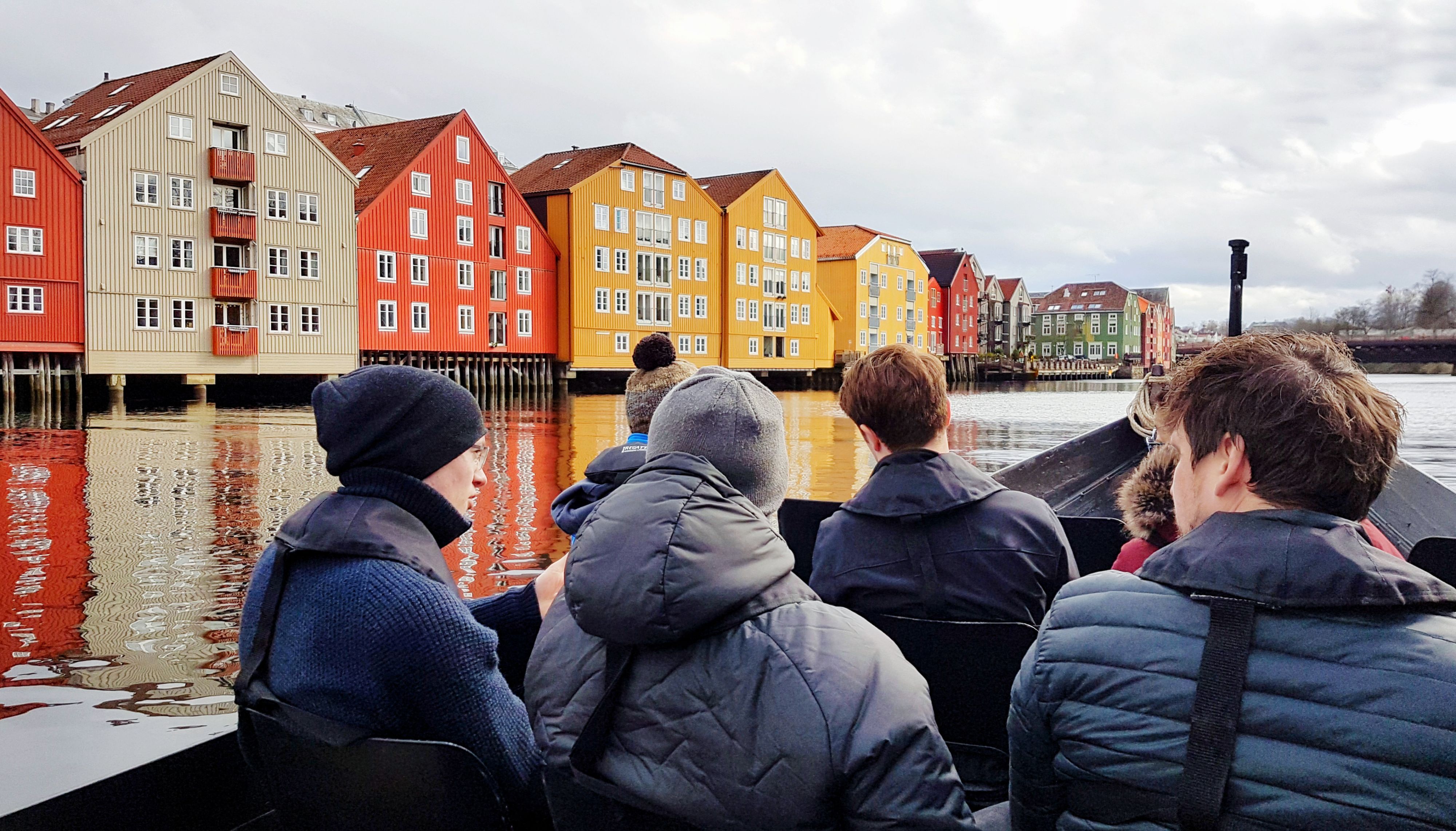 Gäste auf einer winterlichen Bootstour, die an den farbenfrohen alten Speicherhäusern entlang der Nidelva in Trondheim, Norwegen, vorbeifährt