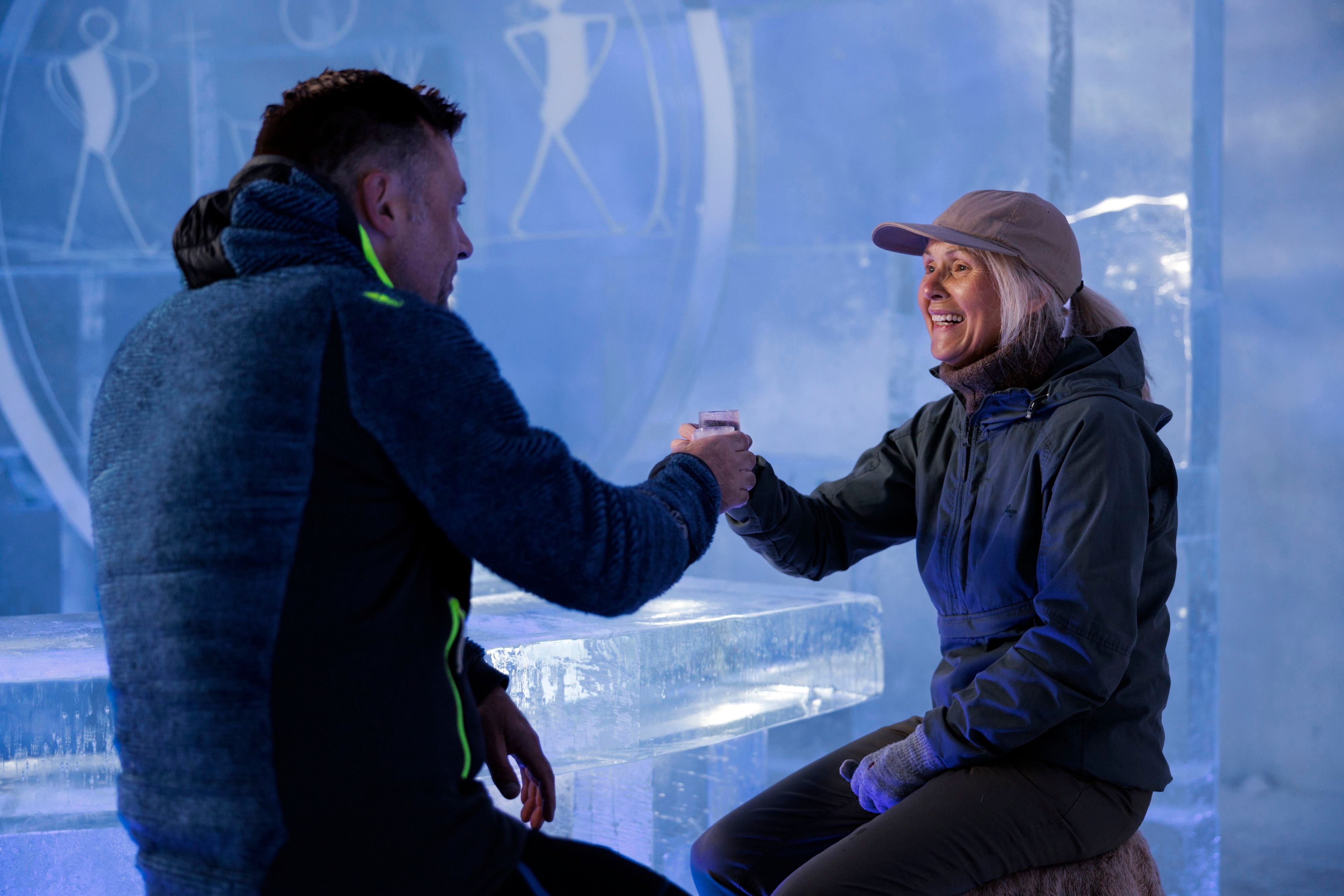 To gjester skåler med isglass mens de sitter ved isbaren inne på Snowhotel Kirkenes.