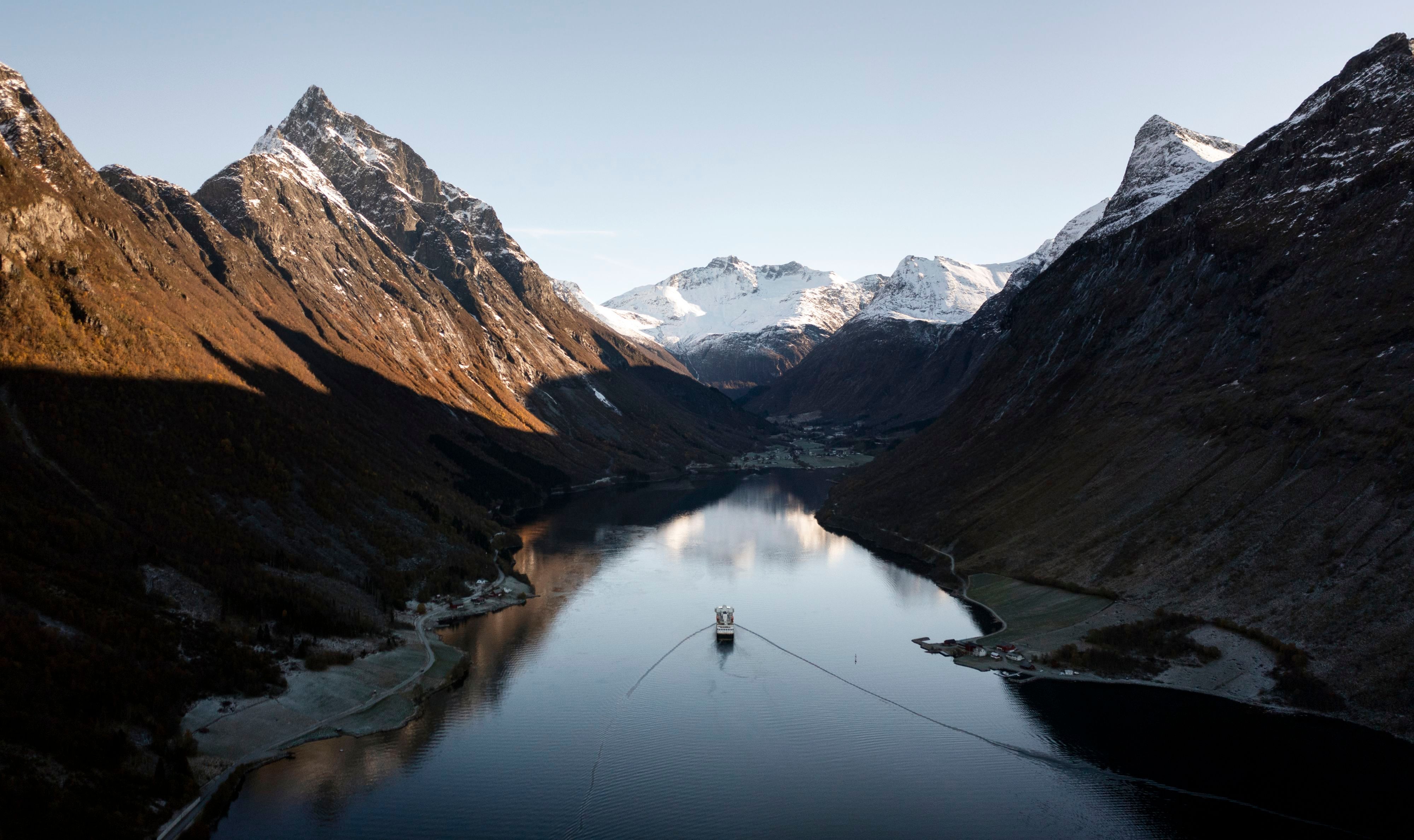 Havila-cruiseskip som seiler gjennom Hjørundfjorden mellom ruvende, snødekte Sunnmørsfjell på en klar septemberdag