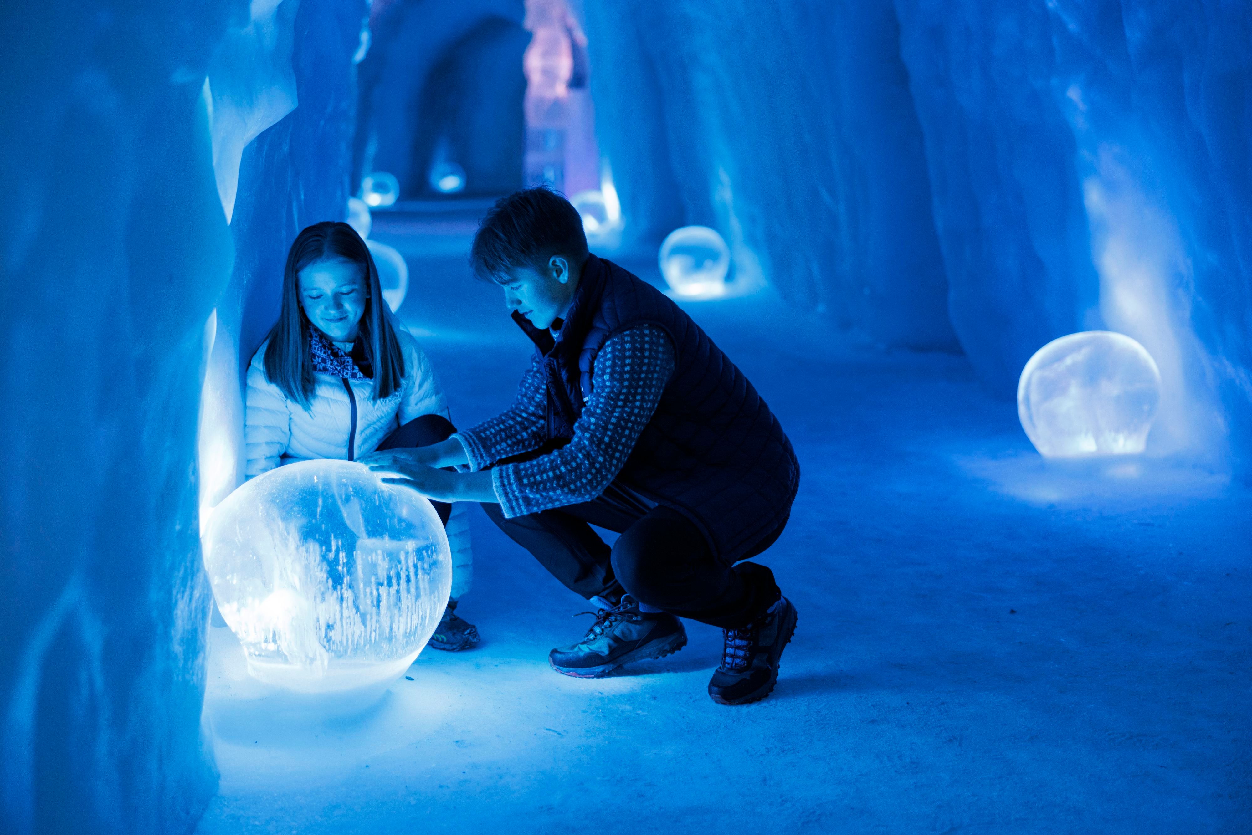 Ett barn och en vuxen som utforskar de glödande isskulpturerna inne på Snowhotel Kirkenes.