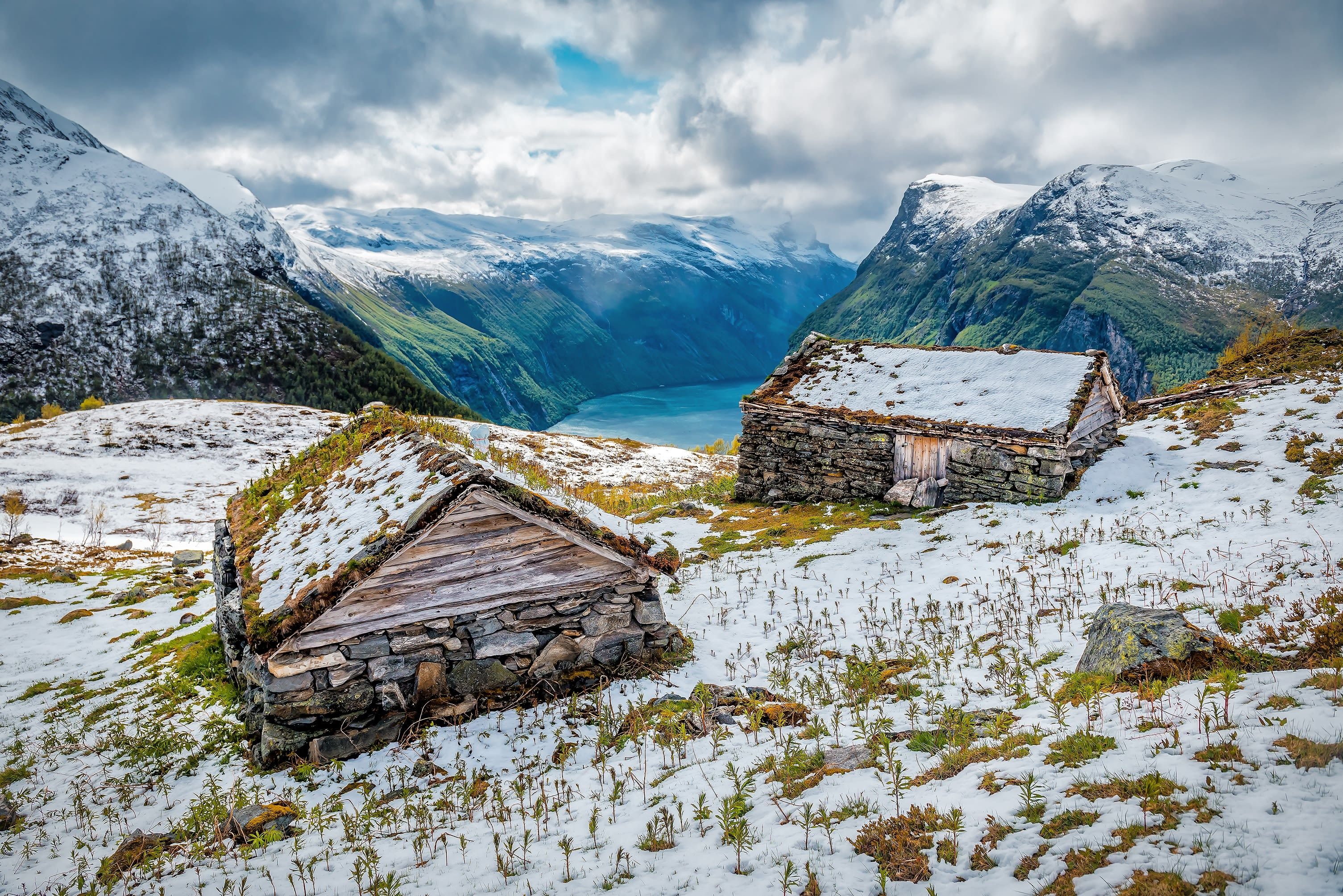 Traditional stone mountain huts with turf roofs above a fjord amid melting snow in early spring (March) in Norway