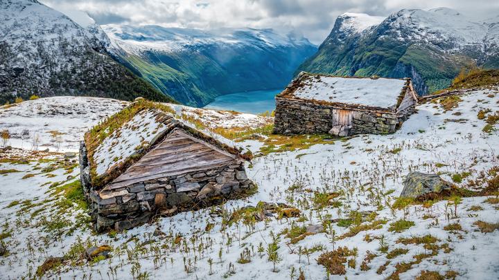 Traditional stone mountain huts with turf roofs above a fjord amid melting snow in early spring (March) in Norway