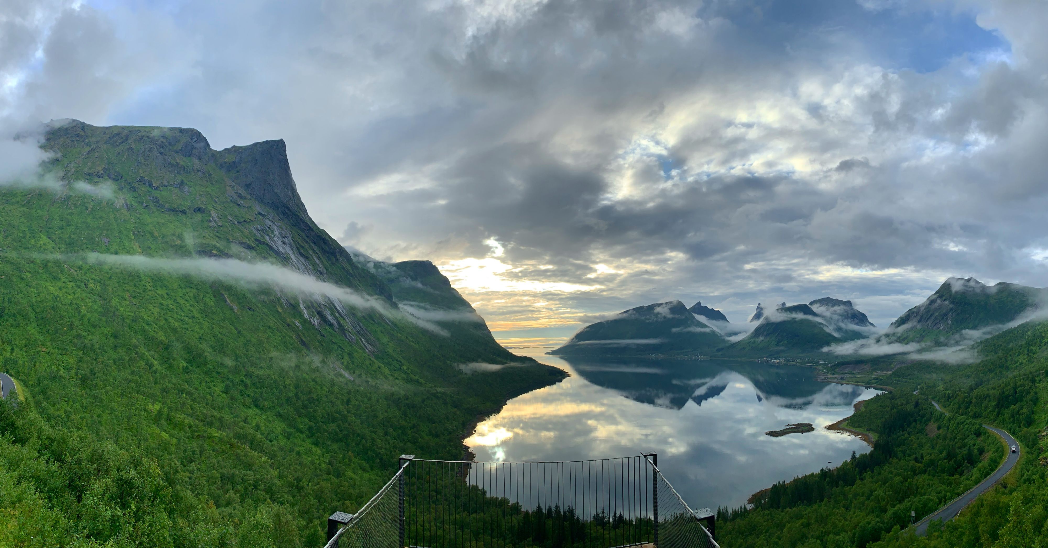 Panoramautsikt fra utsiktspunktet Bergsbotn over Bergsfjorden, omgitt av frodige grønne fjell, rolig arktisk vann og dramatiske skyer på Senja.