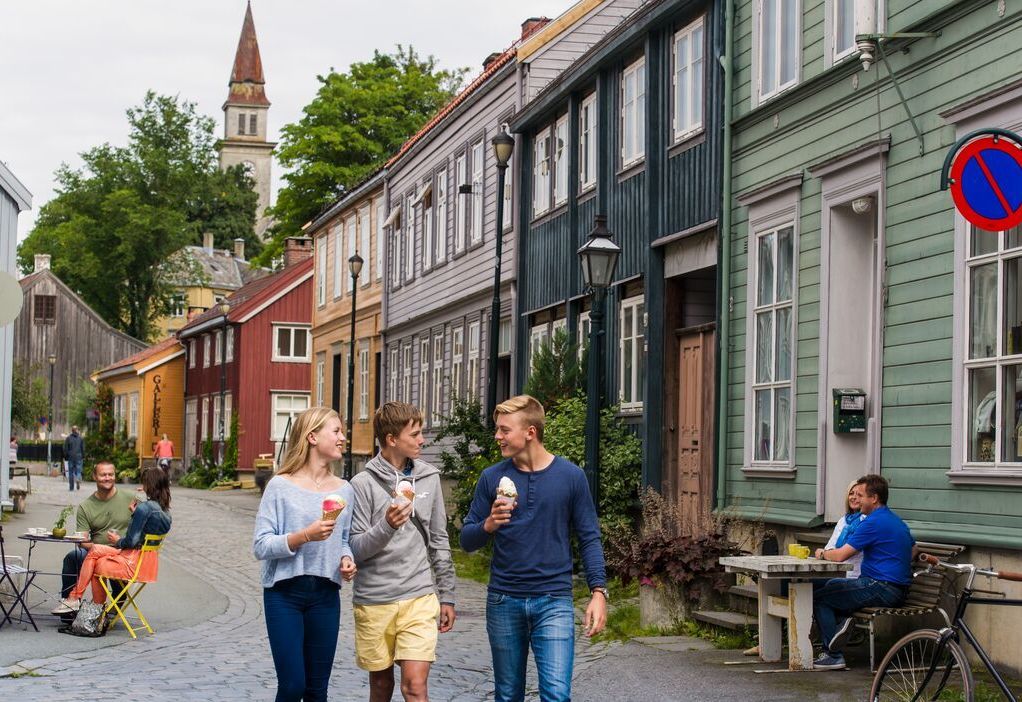 Unge venner med iskrem som går forbi fargerike trehus i Bakklandet i Trondheim, Norge