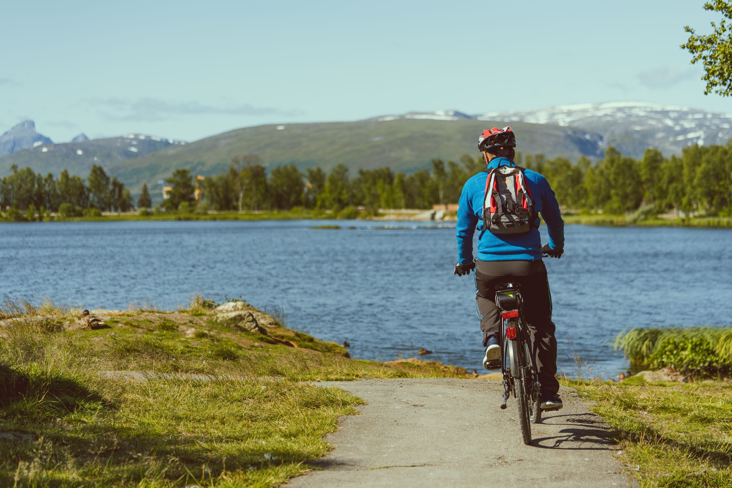 Gjest som sykler langs en naturskjønn innsjø på en guidet elsykkeltur i Tromsø, med arktiske fjell i bakgrunnen.