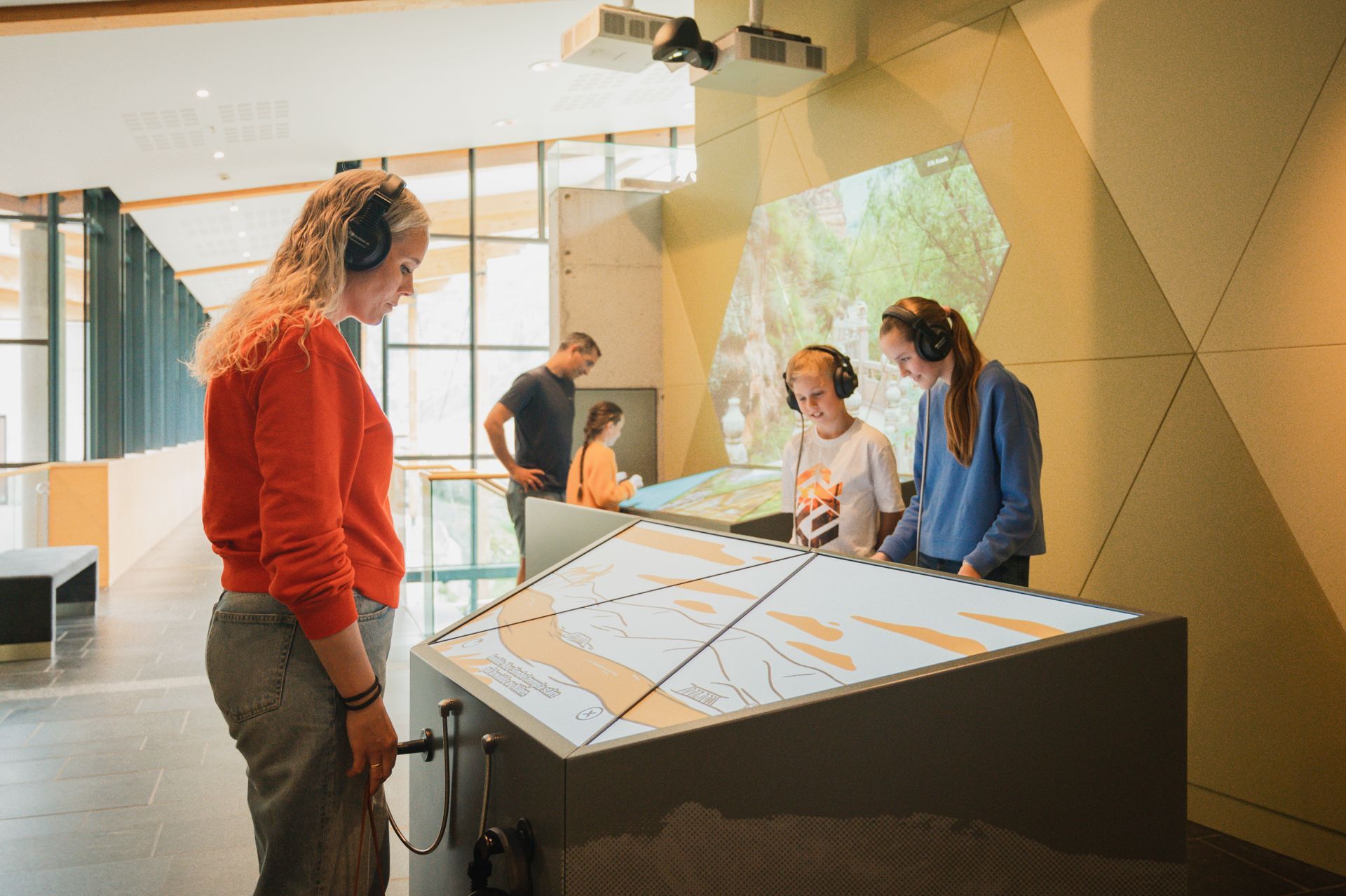 Family with headphones exploring interactive exhibits at the Norwegian Fjord Centre in Geiranger, Norway